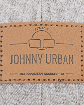 Nahaufnahme eines braunen Lederetiketts mit dem Schriftzug 'JOHNNY URBAN METROPOLITAN ACCESSORIES' auf graubraunem Stoff