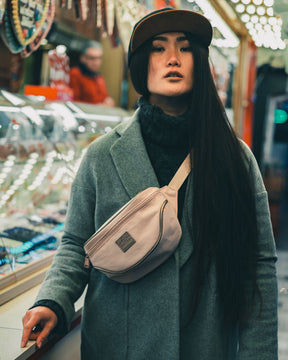Frau mit langem schwarzen Haar trägt rosefarbene Bauchtasche 'Ben' von Johnny Urban im Markt