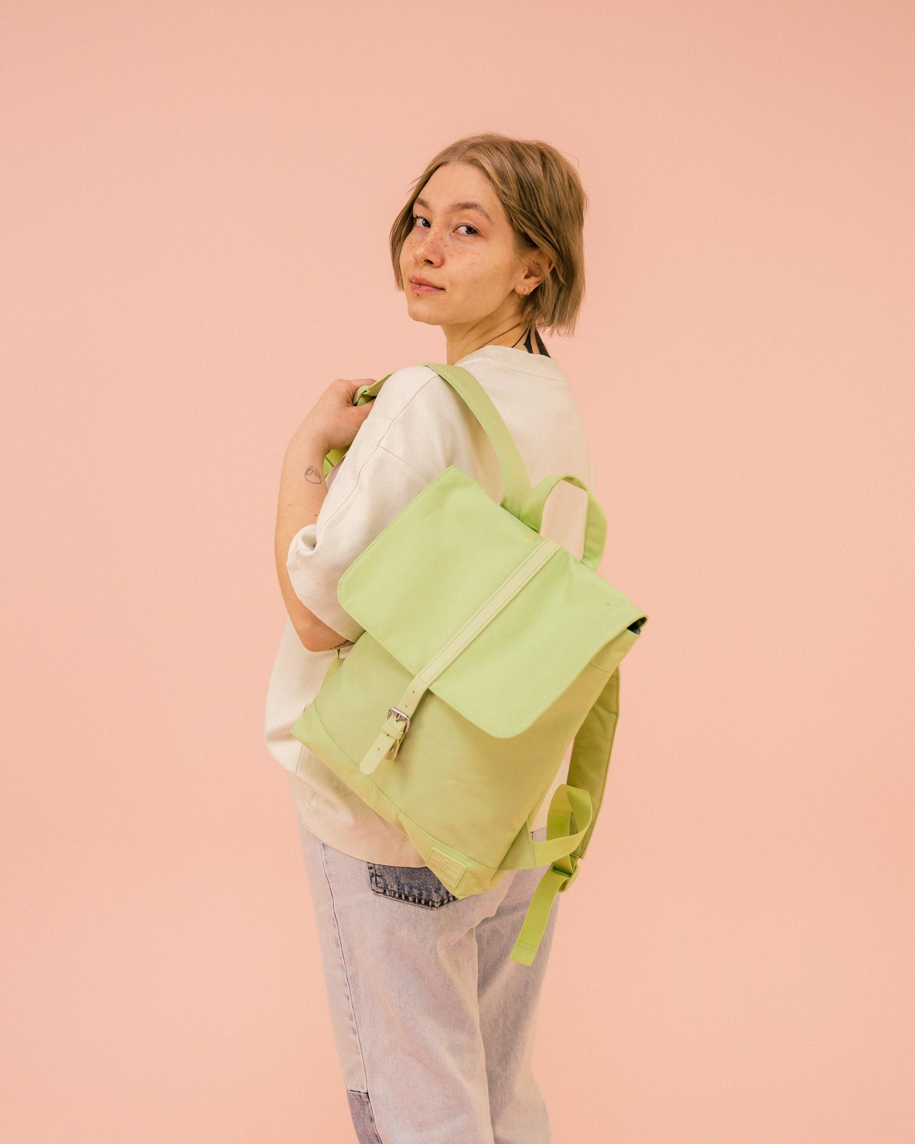 Frau trägt limegrünen Damen-Rucksack 'Mia' von Johnny Urban über dem Schulter, beige Sweatshirt, helle Jeans