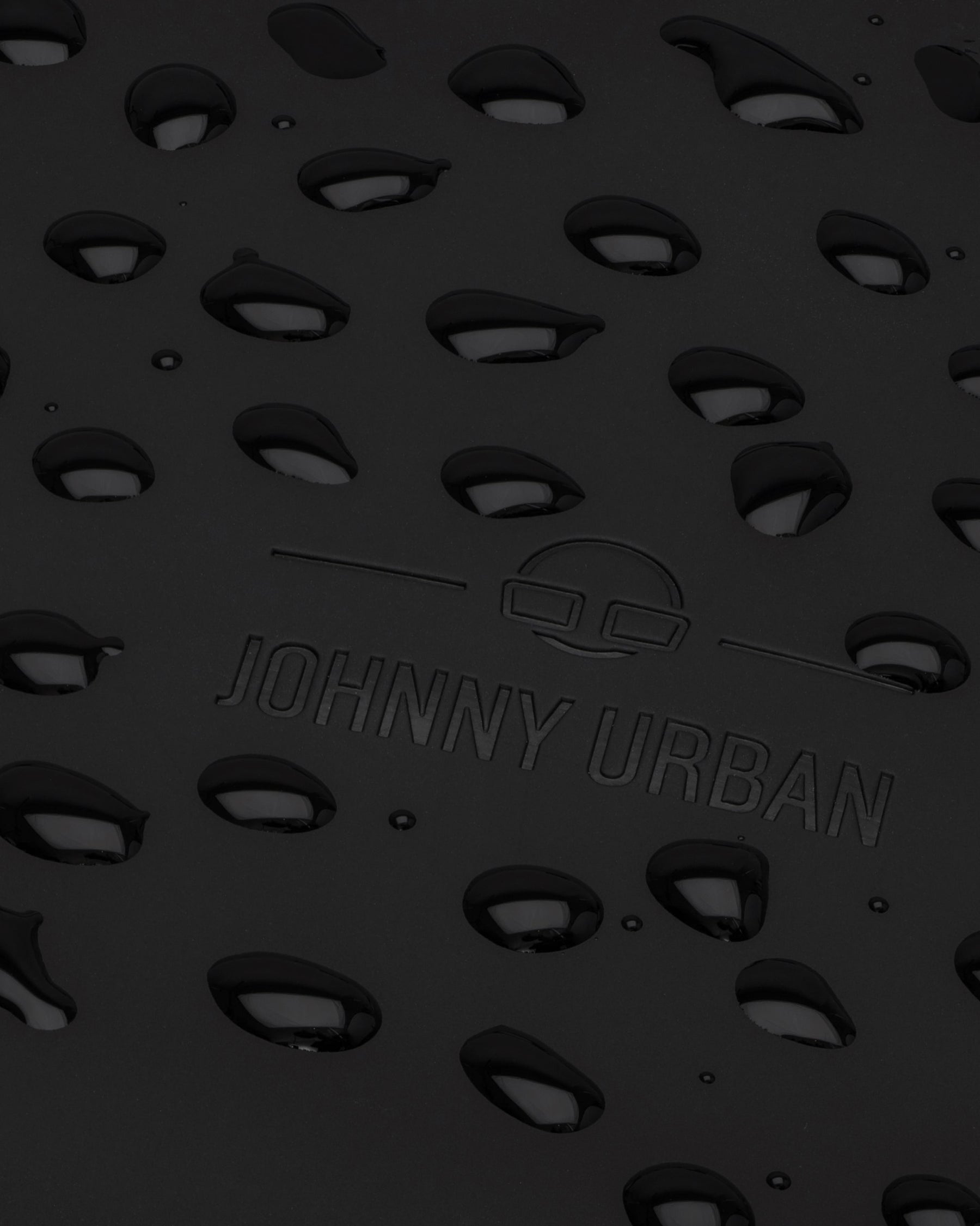 Nahaufnahme des schwarzen, regenfesten Rucksacks 'Hailey' mit JOHNNY URBAN Logo und Wasserperlen auf Oberfläche