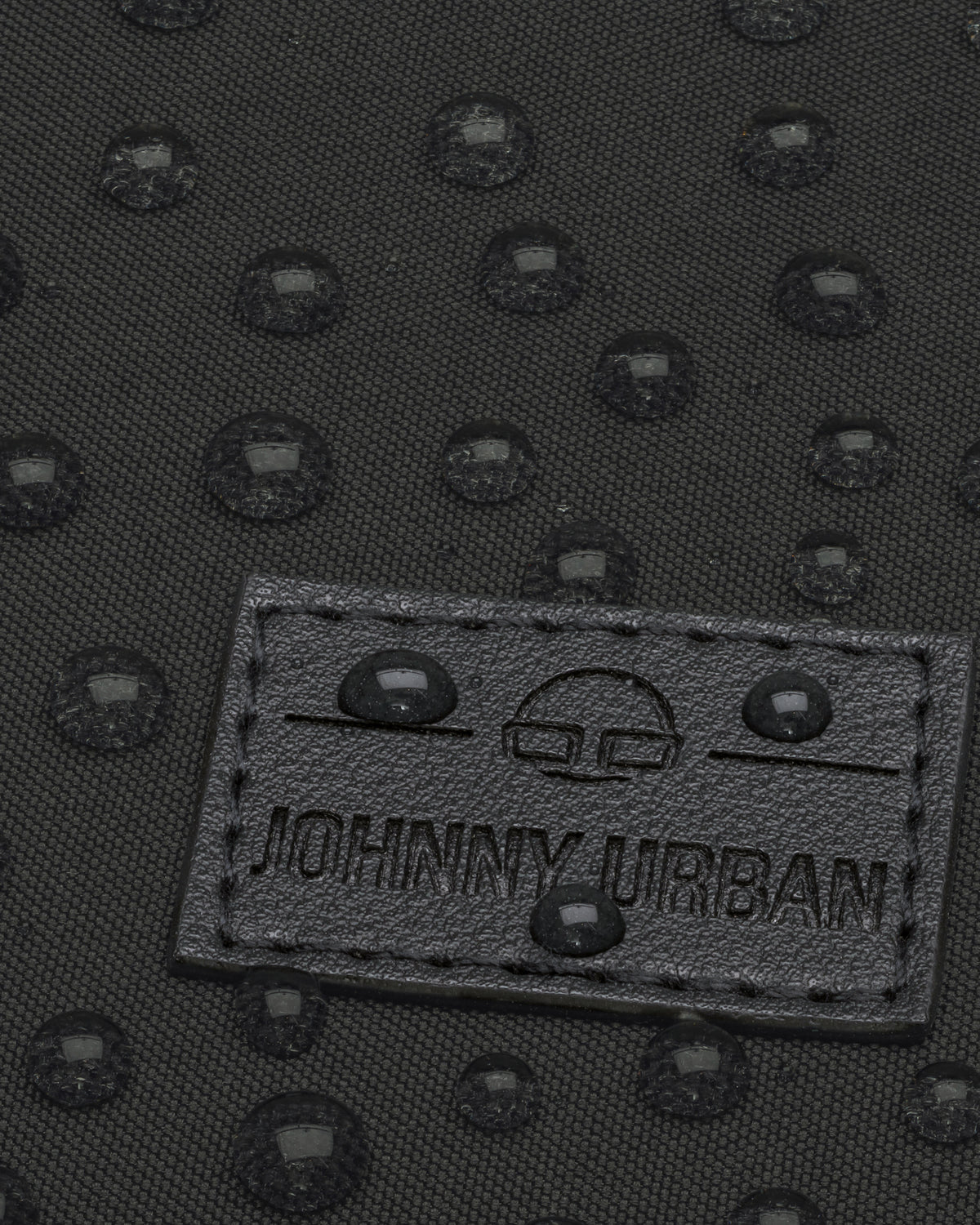 Nahaufnahme des wasserabweisenden schwarzen Stoffs des Rucksacks Jona Small mit Johnny Urban Logo und Wasserperlen