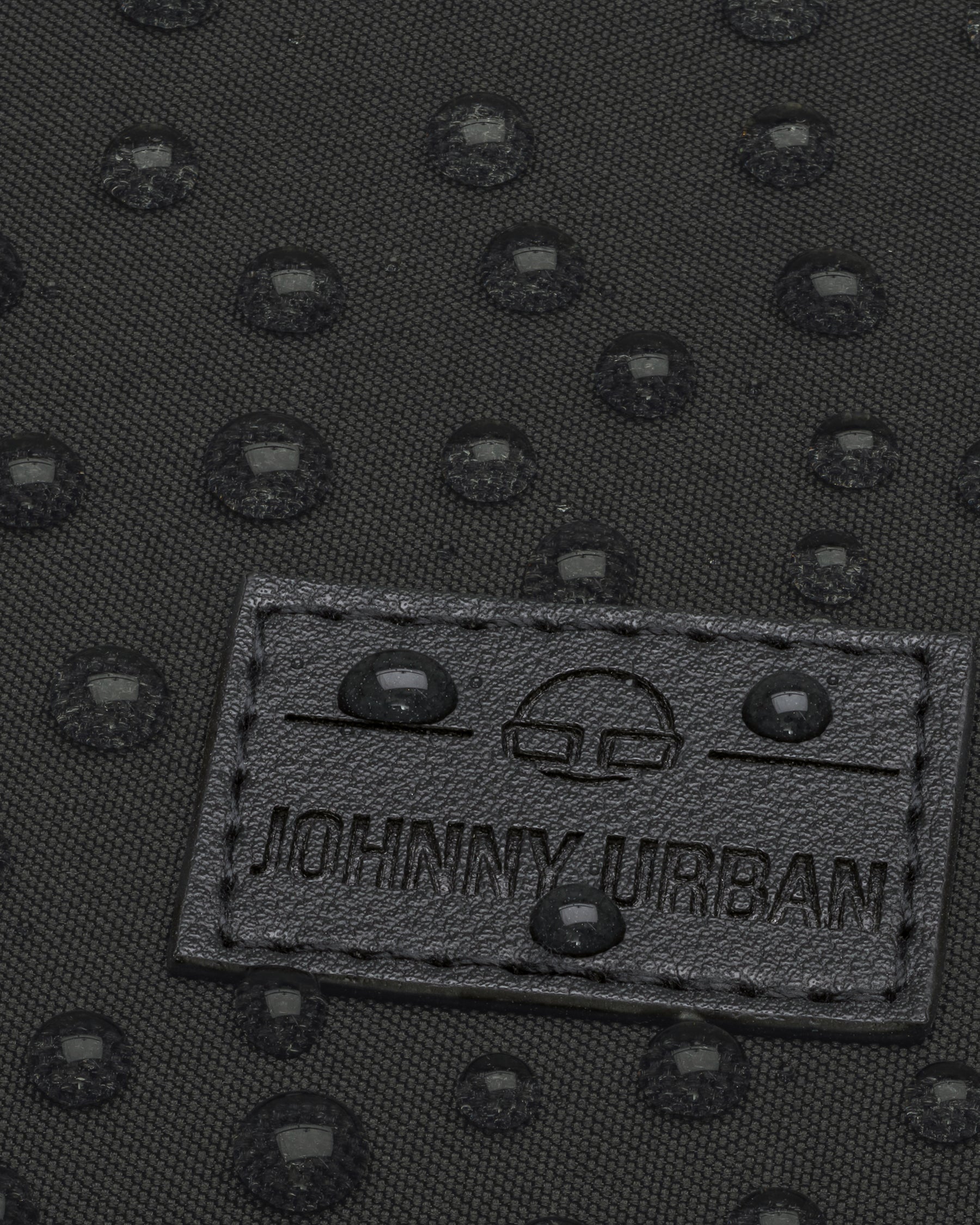 Nahaufnahme des wasserabweisenden schwarzen Stoffs des Rucksacks Jona Small mit Johnny Urban Logo und Wasserperlen