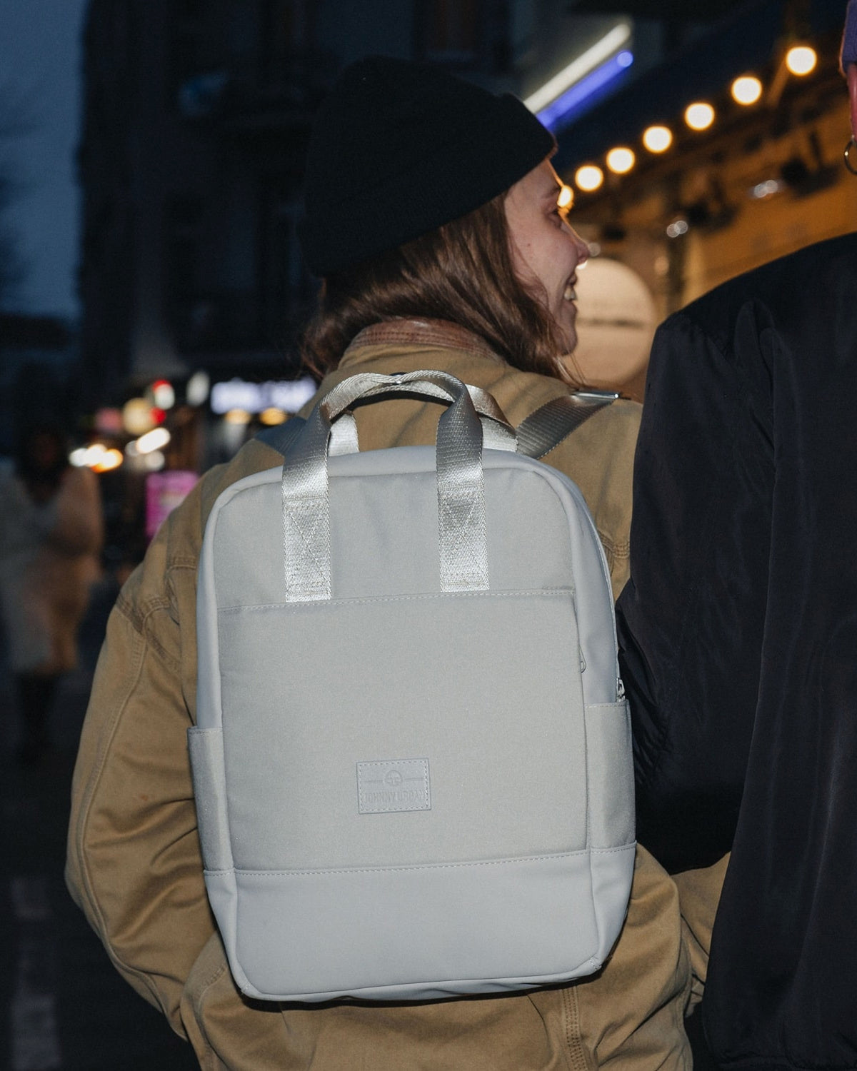 Frau trägt beigen Damenrucksack Jona Medium von Johnny Urban auf Rücken in urbaner Nachtumgebung