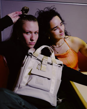 Zwei Frauen sitzen zusammen, eine trägt den beigen Rucksack 'Jules' von Johnny Urban auf dem Schoß