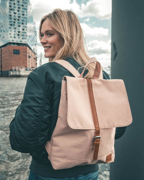Frau mit schwarzer Jacke trägt rosa Damenrucksack 'Mia' von Johnny Urban an einem Hafen mit modernem Gebäude