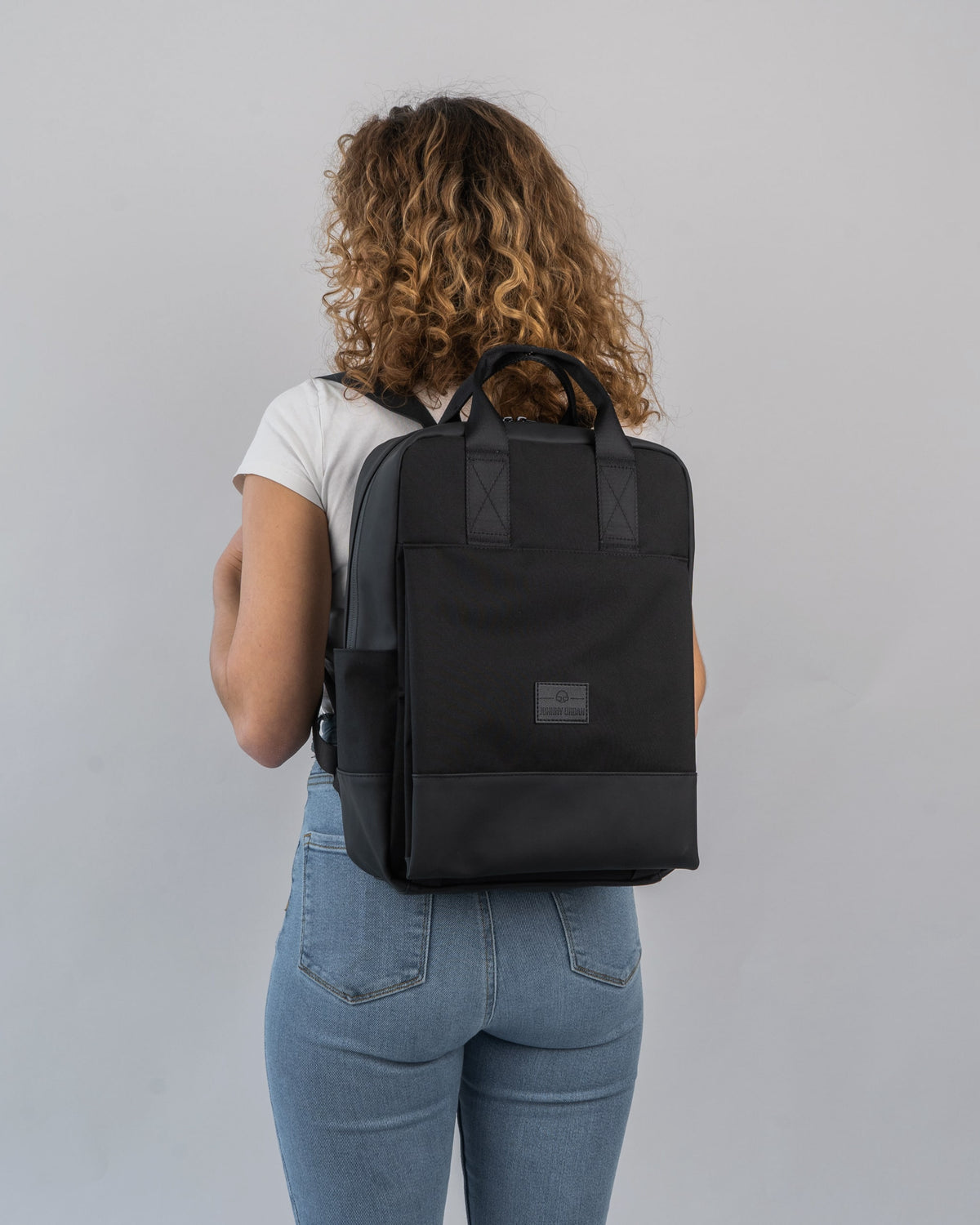 Frau mit lockigen Haaren trägt schwarzen Damenrucksack 'Jona Large' von Johnny Urban, frontal nicht sichtbar