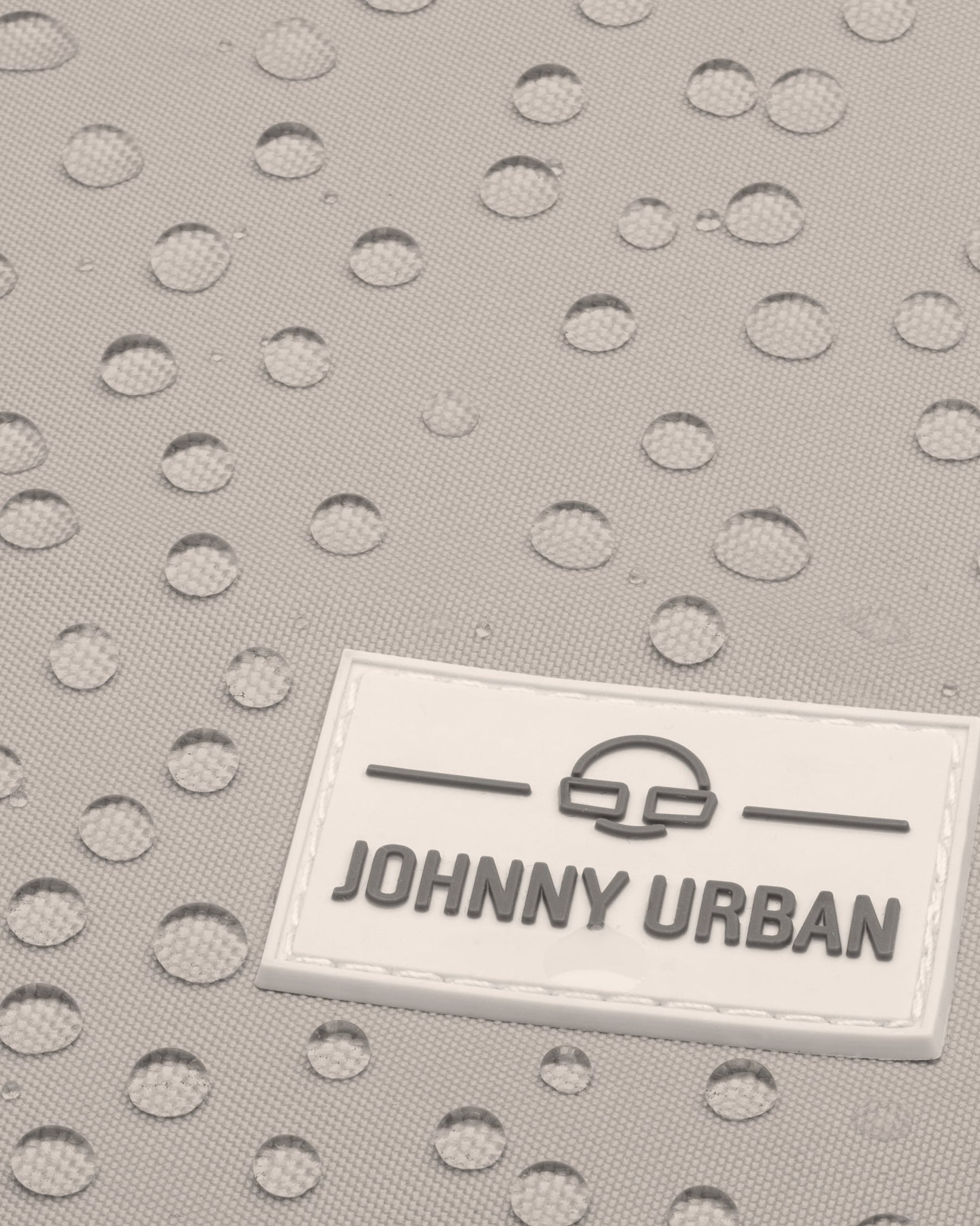 Detail des wasserabweisenden Jona Medium Rucksacks von Johnny Urban mit Wassertropfen auf beige-grauem Stoff