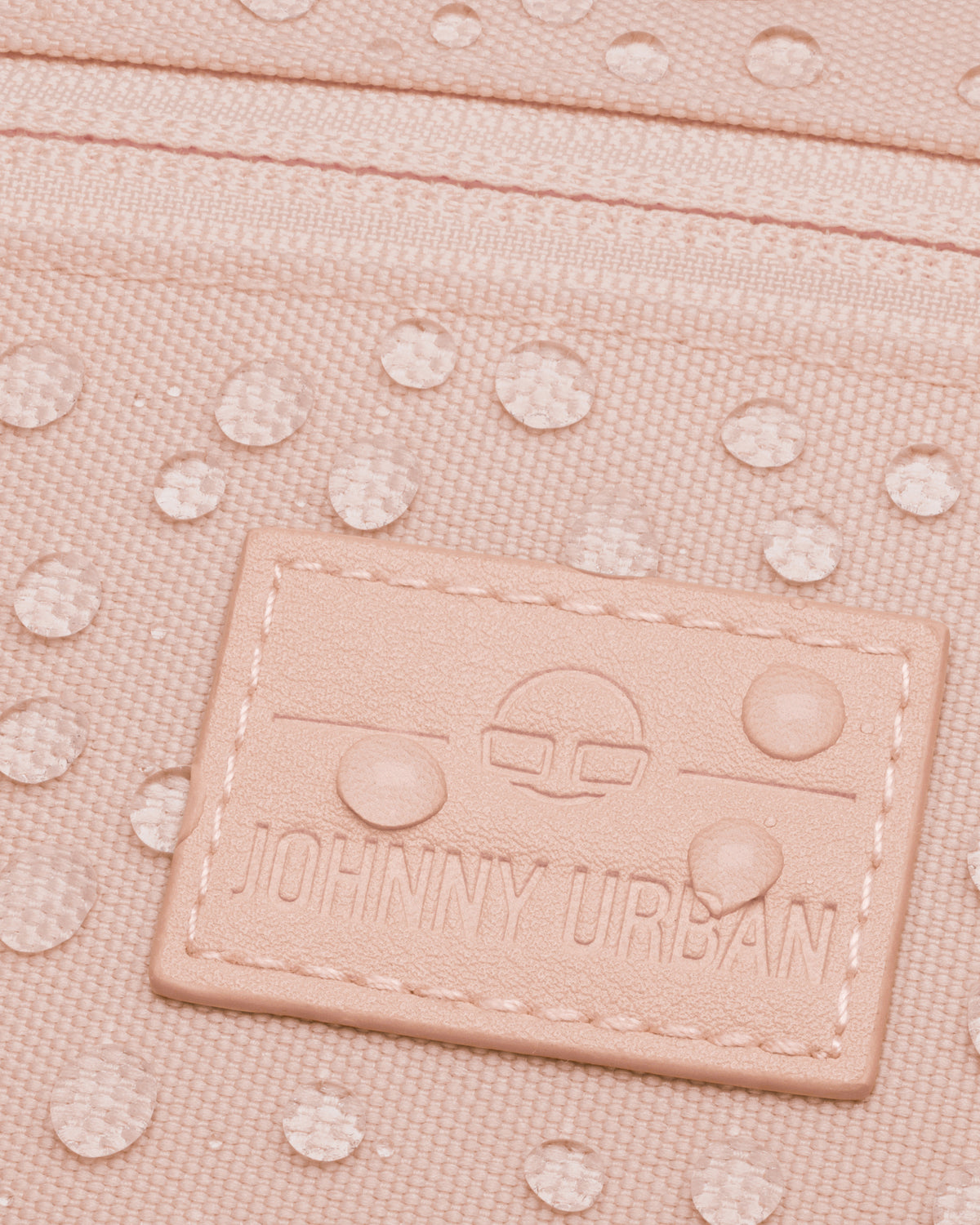 Nahaufnahme der rosa Bauchtasche 'Erik Small' mit Johnny Urban Logo und Wassertropfen auf der Oberfläche