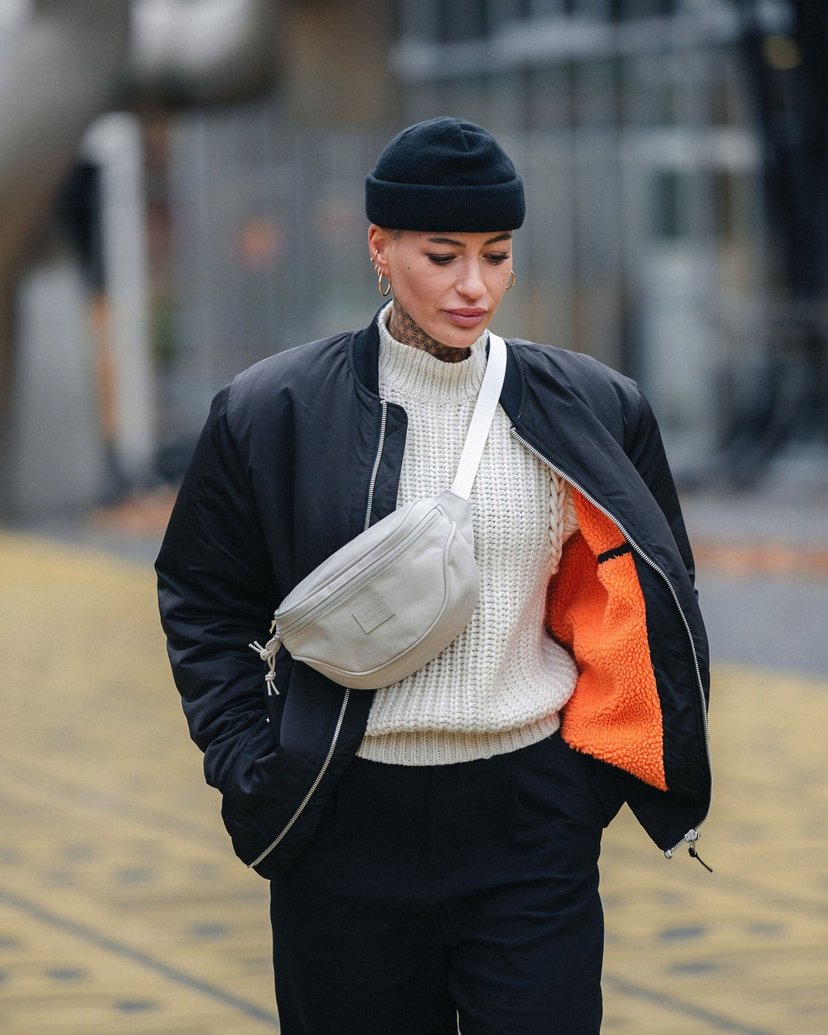 Frau trägt beige Bauchtasche 'Ben' über einem weißen Strickpullover und schwarzer Jacke mit orangem Innenfutter