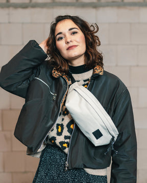Frau trägt beige Bauchtasche 'Tom' von Johnny Urban über einem schwarzen, kurz geschnittenen Mantel und Animal-Print-Pullover