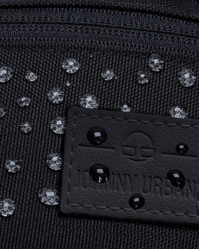 Nahe Aufnahme einer wasserabweisenden schwarzen Bauchtasche 'Erik Small' mit Wassertropfen auf dem Stoff und dem Johnny Urban Label