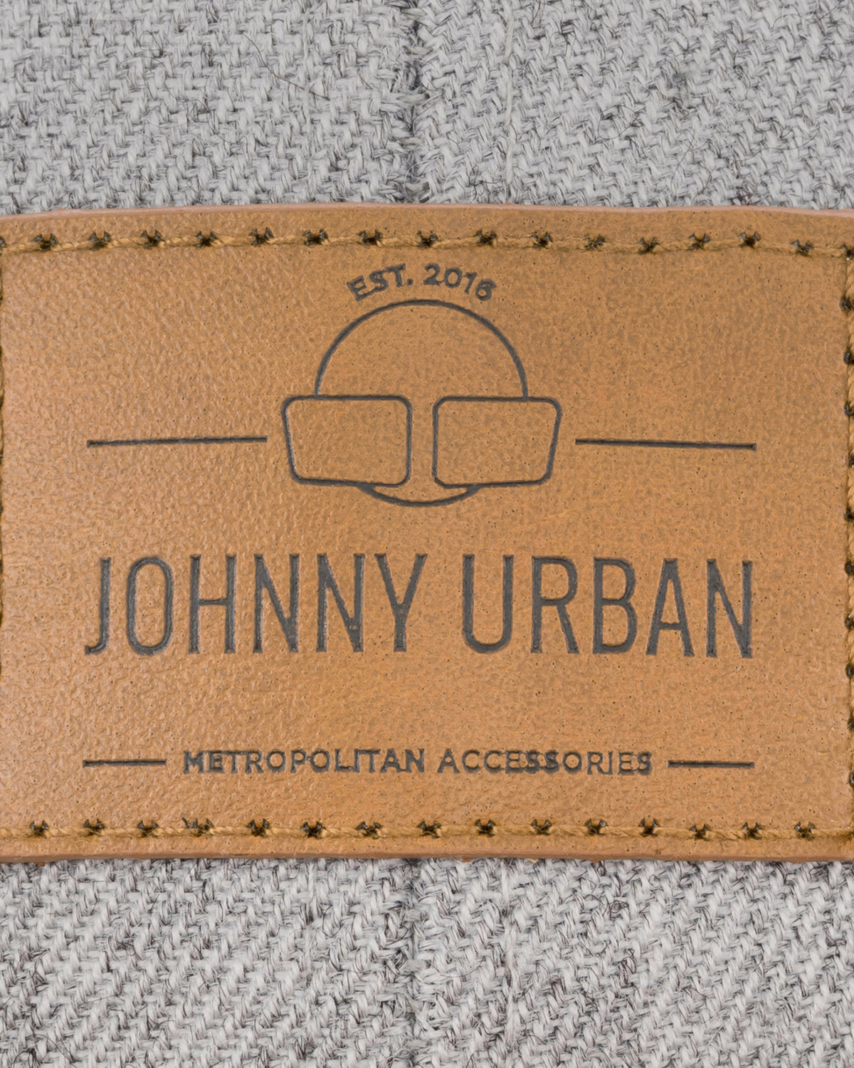 Nahtloses braunes Lederetikett mit Johnny Urban-Logo und Schriftzug auf grauer Textilstruktur