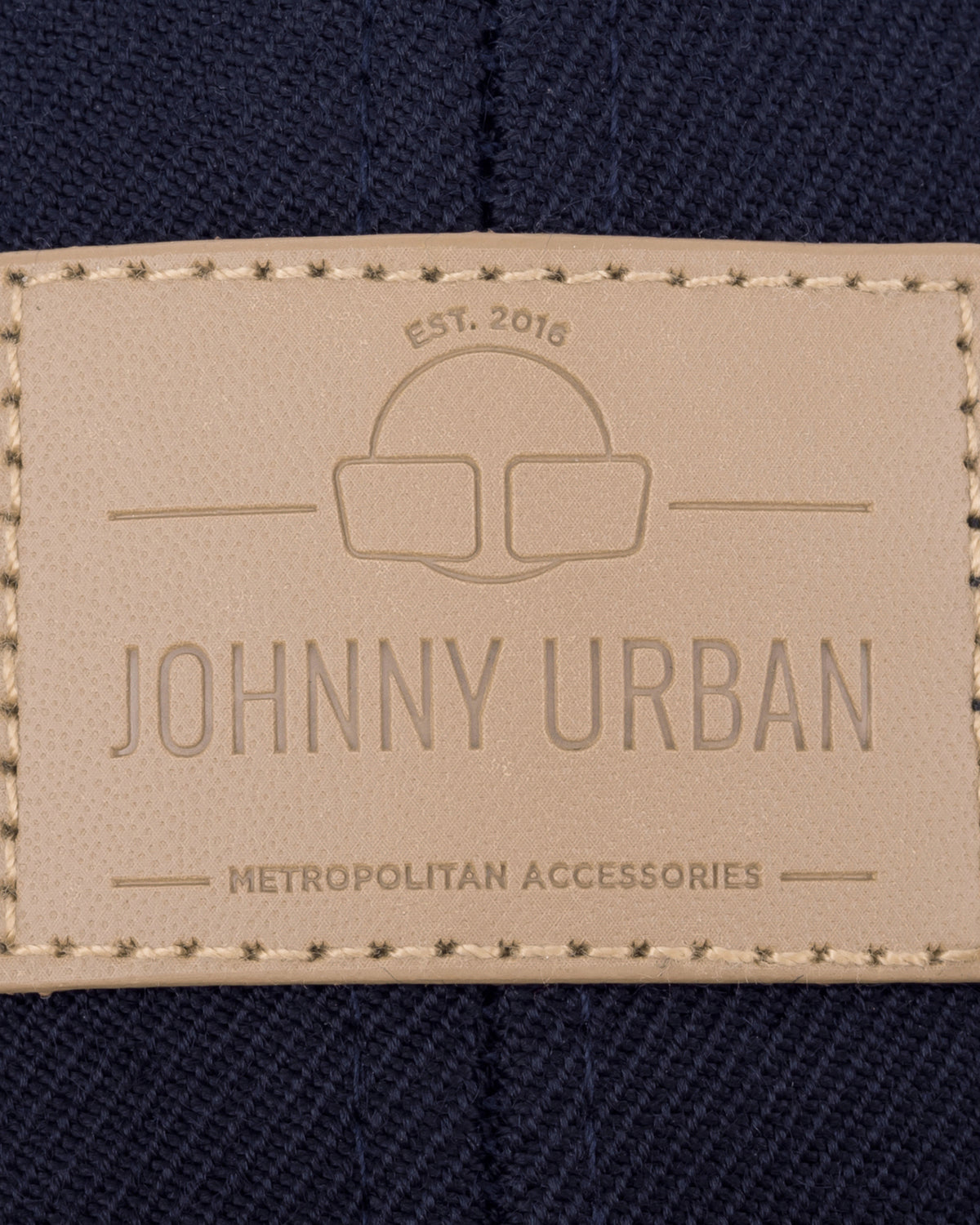 Beige geprägtes Lederetikett mit 'Johnny Urban', 'EST. 2016' und 'Metropolitan Accessories' auf dunkelblauem Stoff