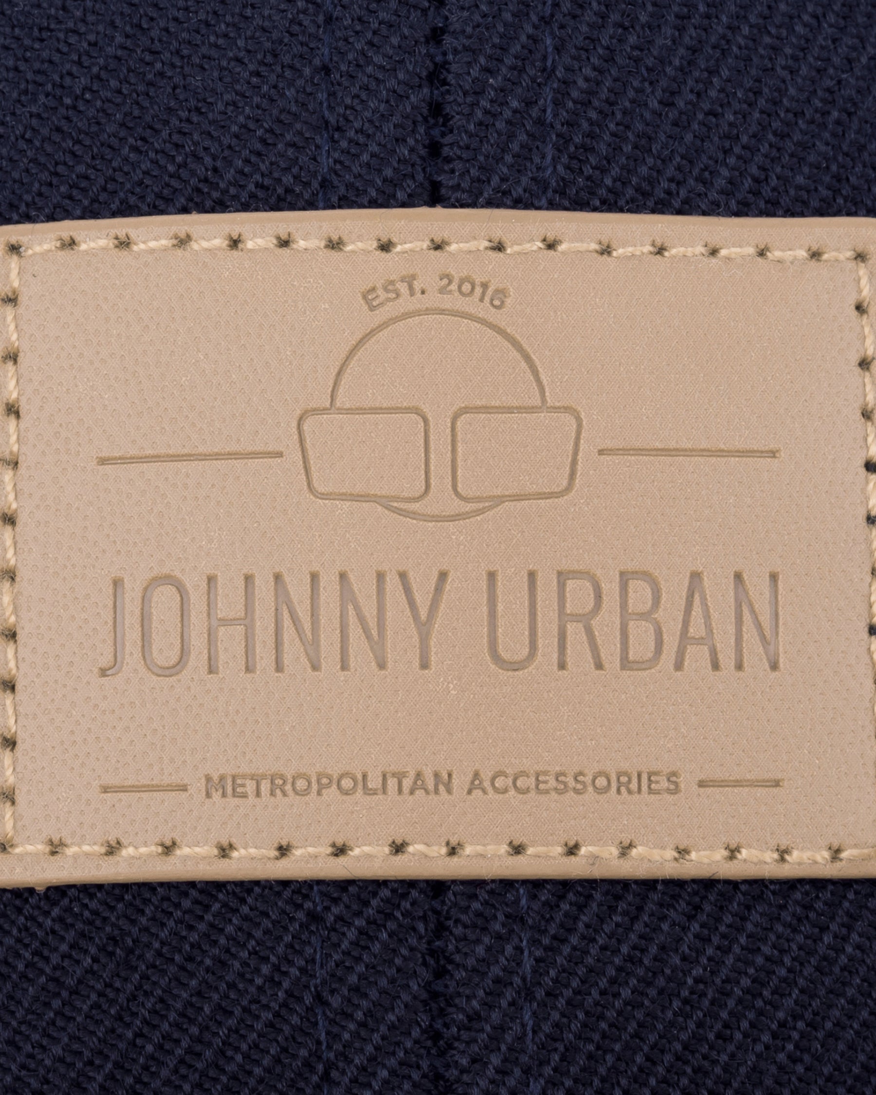 Beige geprägtes Lederetikett mit 'Johnny Urban', 'EST. 2016' und 'Metropolitan Accessories' auf dunkelblauem Stoff
