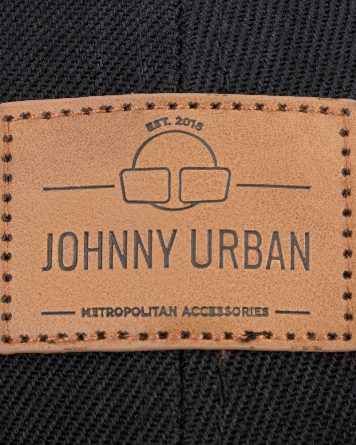 Nahaufnahme eines braunen, rechteckigen Johnny Urban Lederlabels mit gesticktem Rand auf schwarzem Stoff