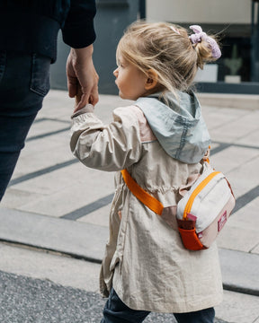 Kindermädchen mit hochgestecktem Haar hält die Hand eines Erwachsenen und trägt die Kinder Bauchtasche 'Felix' in Beige mit orangefarbenen Akzenten