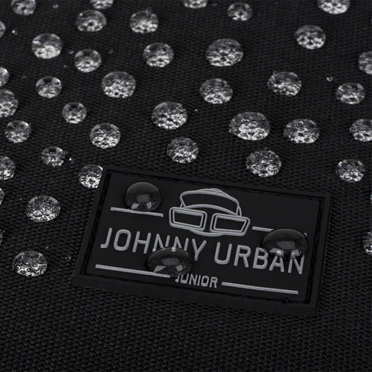 Detail des wasserabweisenden Johnny Urban Junior Kinderrucksacks 'Liam' mit Wasserperlen auf schwarzem Stoff