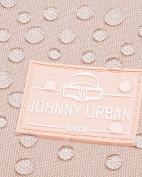 Nahaufnahme des rosa Johnny Urban Junior Logos auf wasserdichtem Stoff mit Wassertropfen