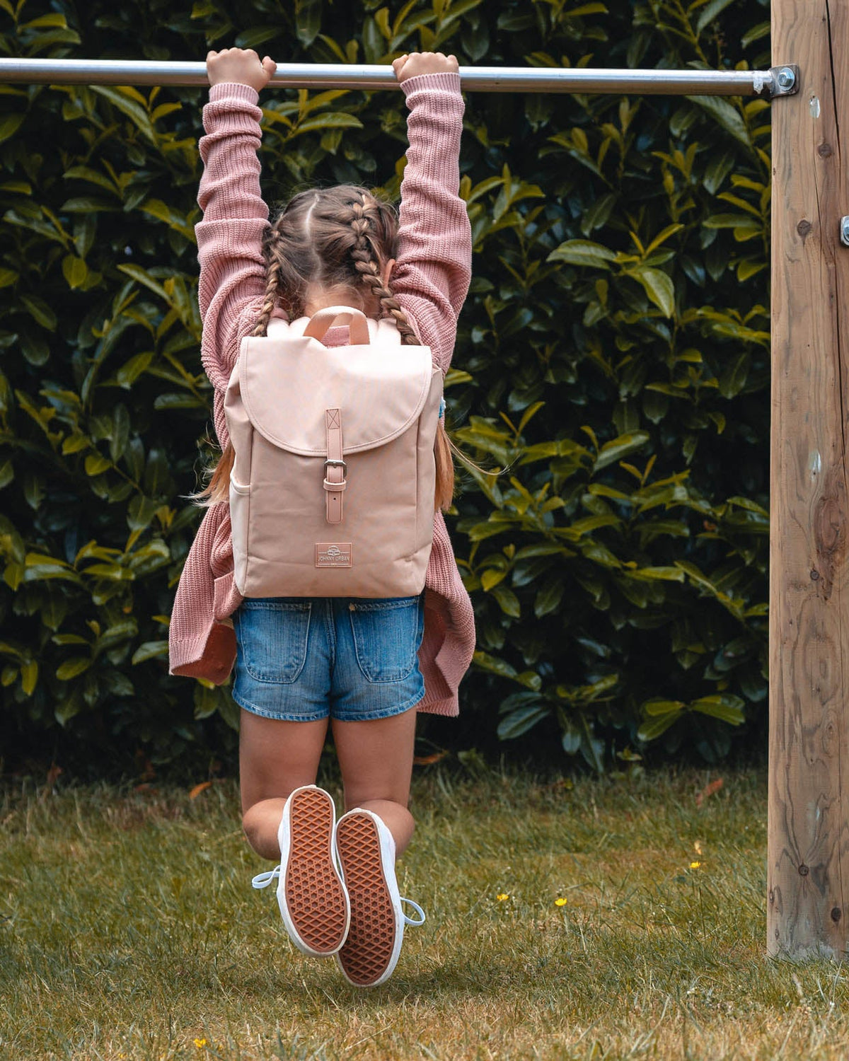 Mädchen mit Kinderrucksack 'Liam' in Rose-klettert an Stange im Garten