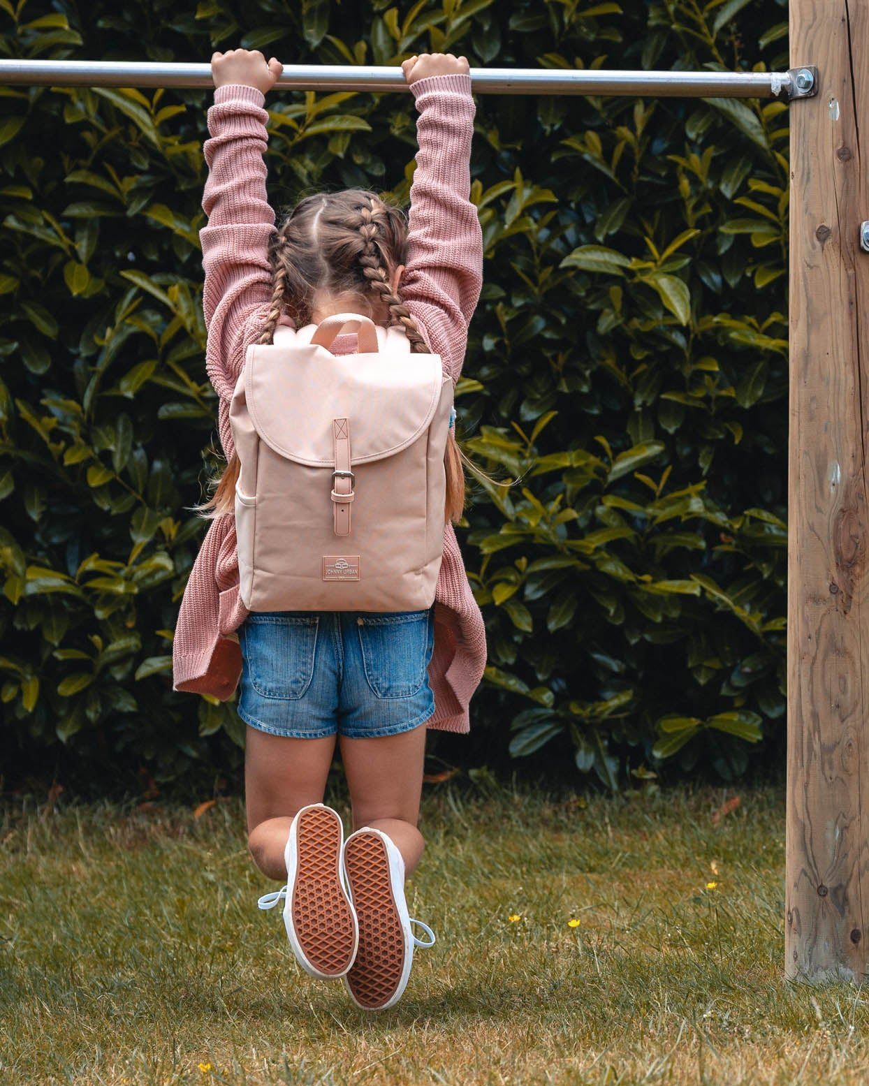 Mädchen mit Kinderrucksack 'Liam' in Rose-klettert an Stange im Garten