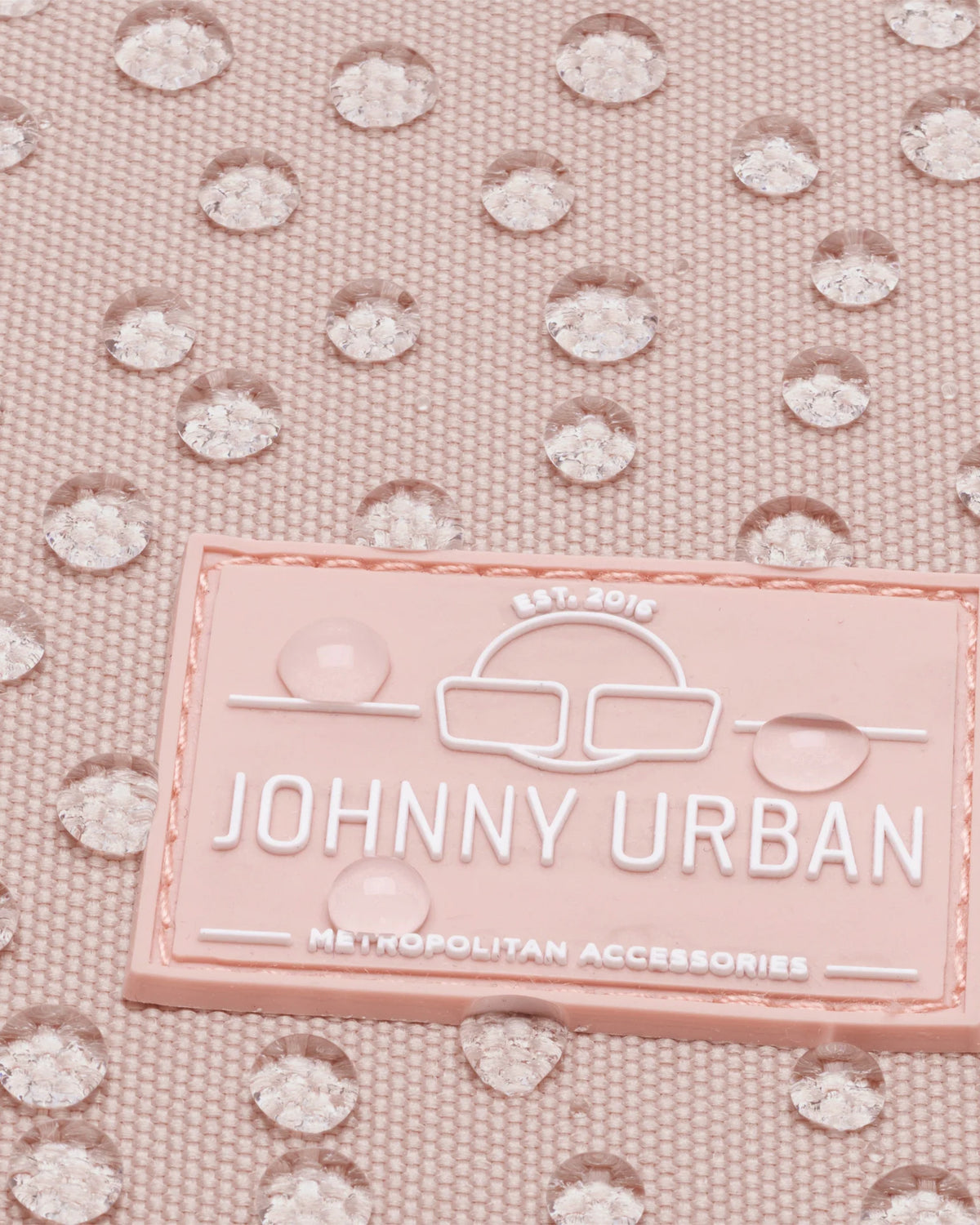 Nahaufnahme des JOHNNY URBAN Logos auf einem rosa wasserdichten Damenrucksack Romy mit Wassertropfen