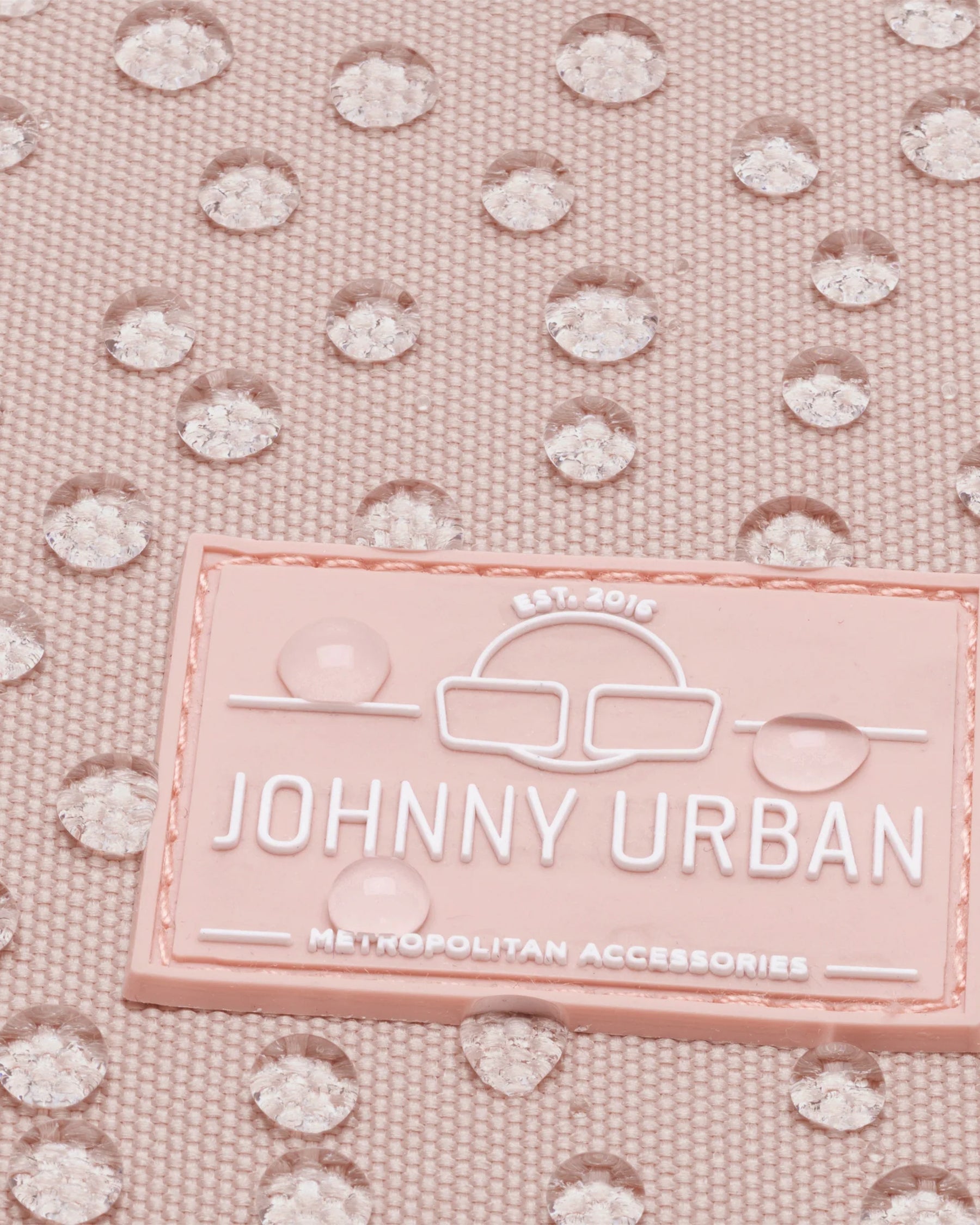 Nahaufnahme des JOHNNY URBAN Logos auf einem rosa wasserdichten Damenrucksack Romy mit Wassertropfen