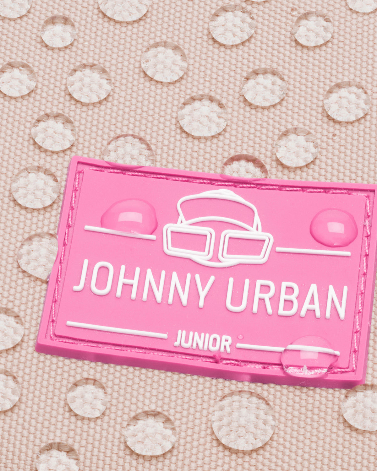 Nahaufnahme des rosa Johnny Urban Junior Logos auf wasserabweisendem Stoff mit Wassertropfen
