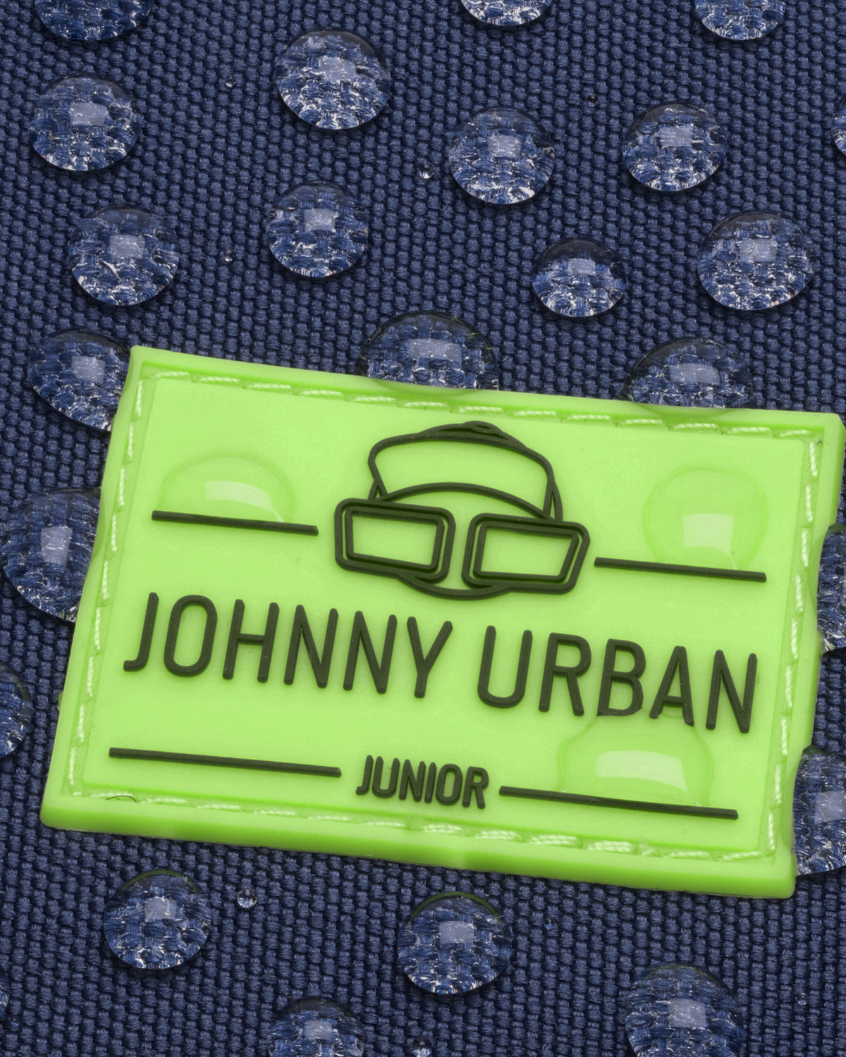 Grünes Johnny Urban Junior Etikett auf blauem wasserdichtem Stoff mit Wassertröpfchen