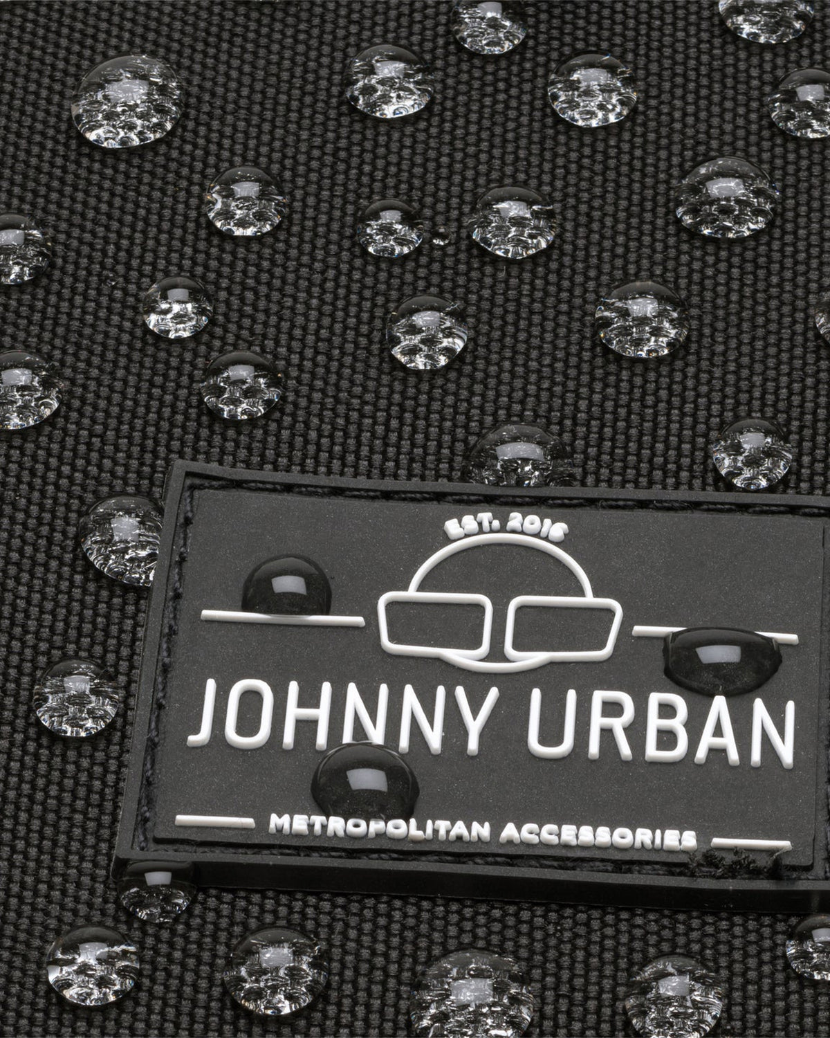 Nahaufnahme des Johnny Urban Logos auf wasserdichtem schwarzen Gewebe mit Wasserperlen