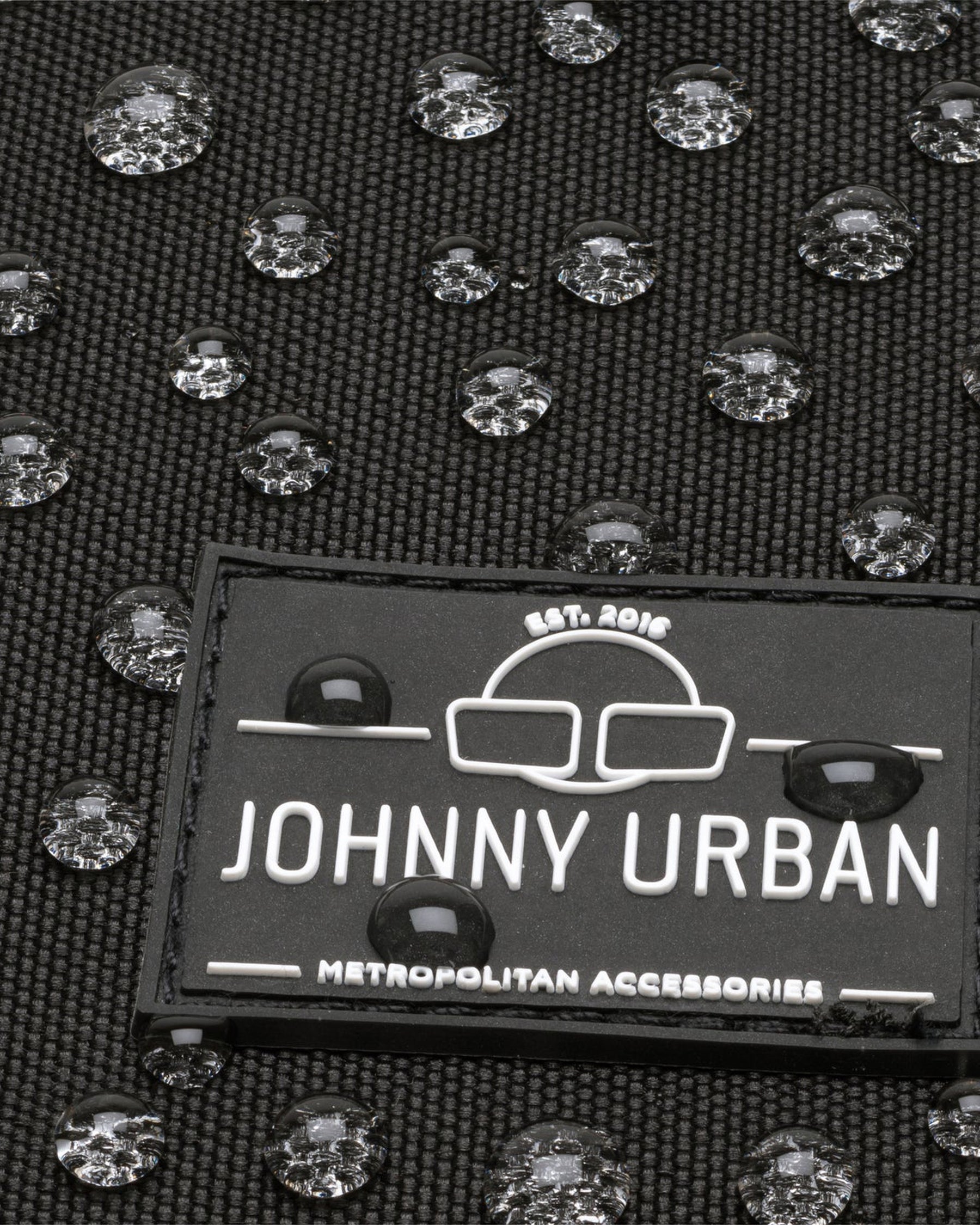 Nahaufnahme des Johnny Urban Logos auf wasserdichtem schwarzen Gewebe mit Wasserperlen