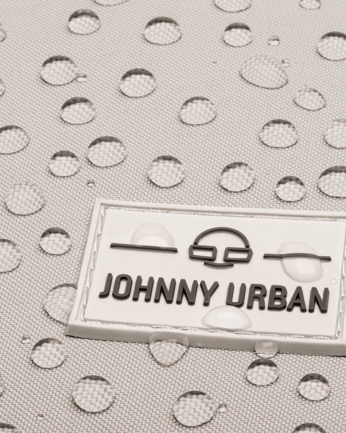 Nahaufnahme des wasserabweisenden Materials des sandgrauen Rucksacks 'Jona Small' mit Johnny Urban Logo
