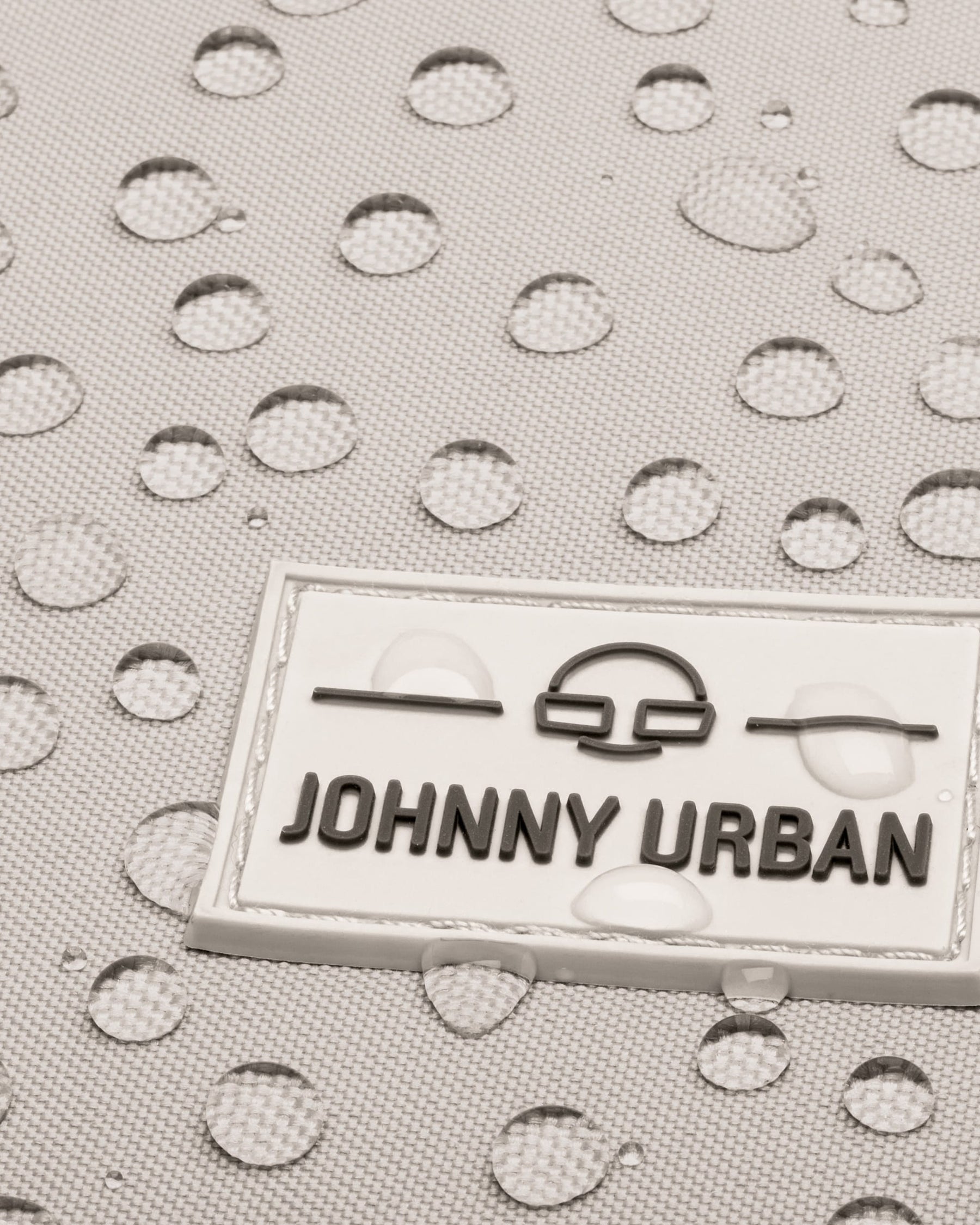 Nahaufnahme des wasserabweisenden Materials des sandgrauen Rucksacks 'Jona Small' mit Johnny Urban Logo