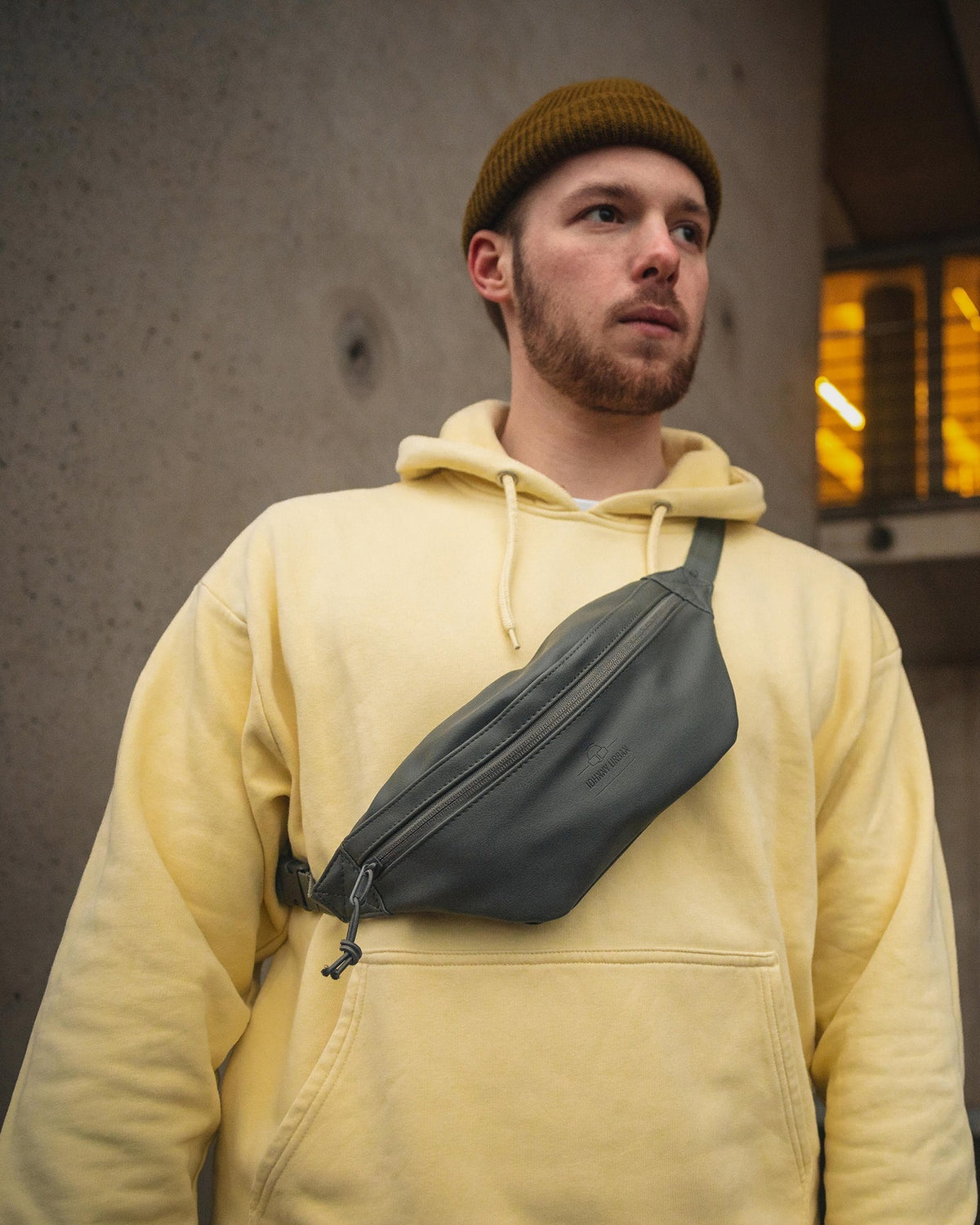 Mann mit gelbem Hoodie und brauner Mütze trägt graue Kunstleder-Bauchtasche "Toni" von Johnny Urban quer über die Brust