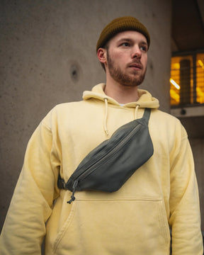 Mann mit gelbem Hoodie und brauner Mütze trägt graue Kunstleder-Bauchtasche "Toni" von Johnny Urban quer über die Brust