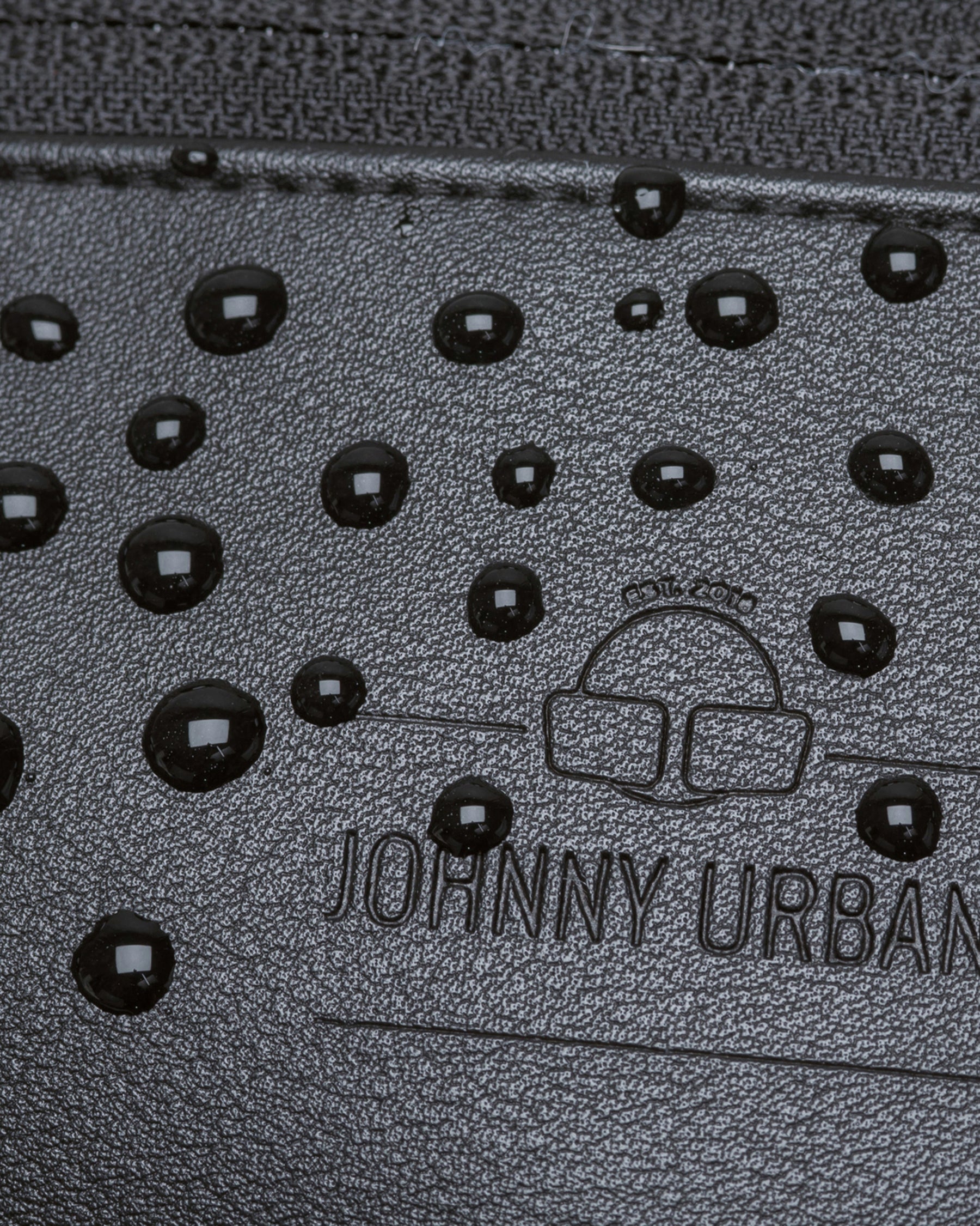Nahaufnahme der wasserabweisenden schwarzen Kunstleder-Bauchtasche 'Toni' von Johnny Urban mit Wasserperlen auf der Oberfläche