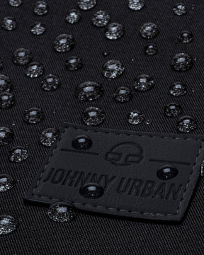 Nahe Aufnahme des schwarzen Labels des Johnny Urban Rucksacks Jona Large mit Wassertropfen auf schwarzem Stoff