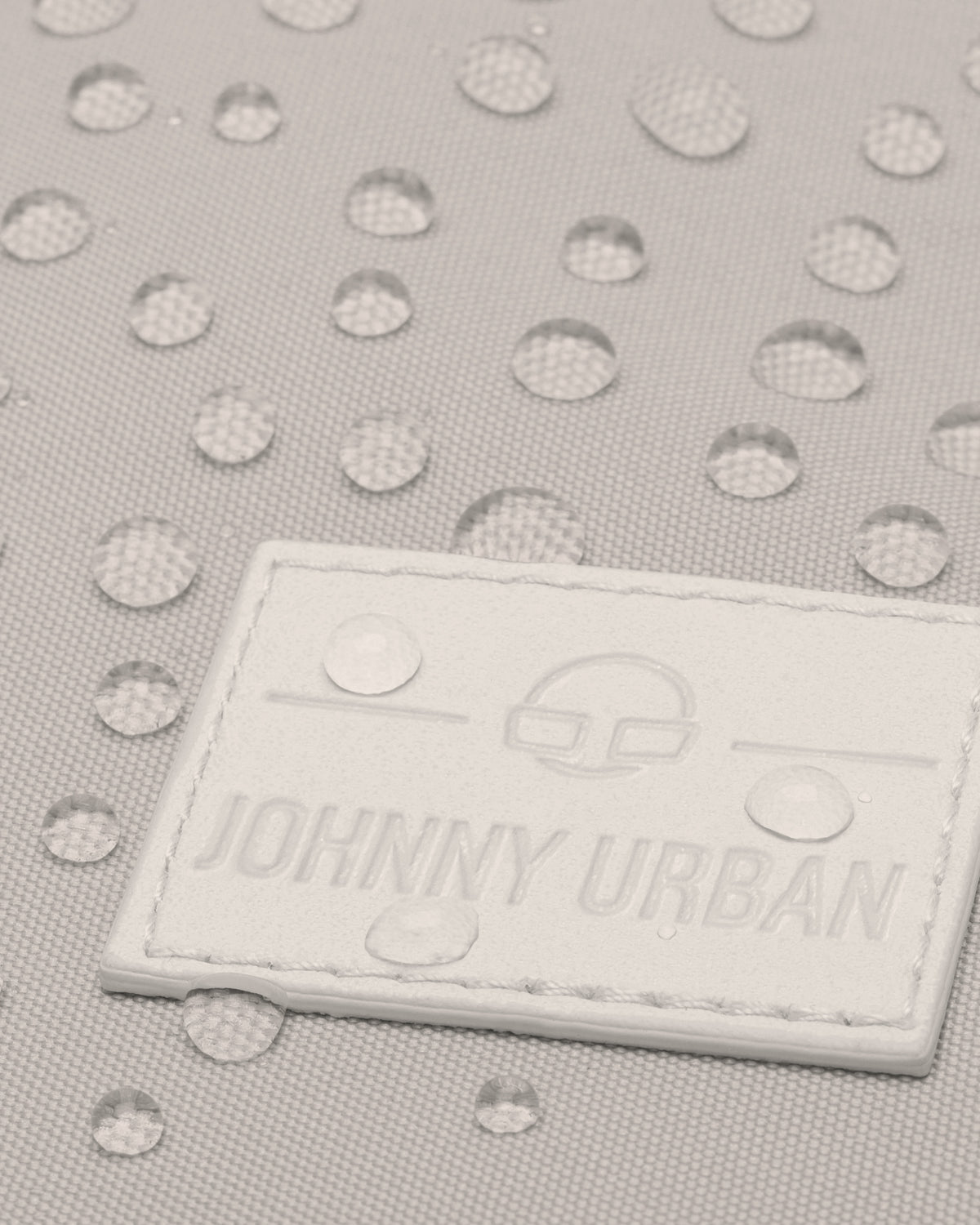 Nahaufnahme des beigen Rucksacks 'Jona Large' mit Wasserperlen auf wasserabweisendem Stoff und Johnny Urban Logo