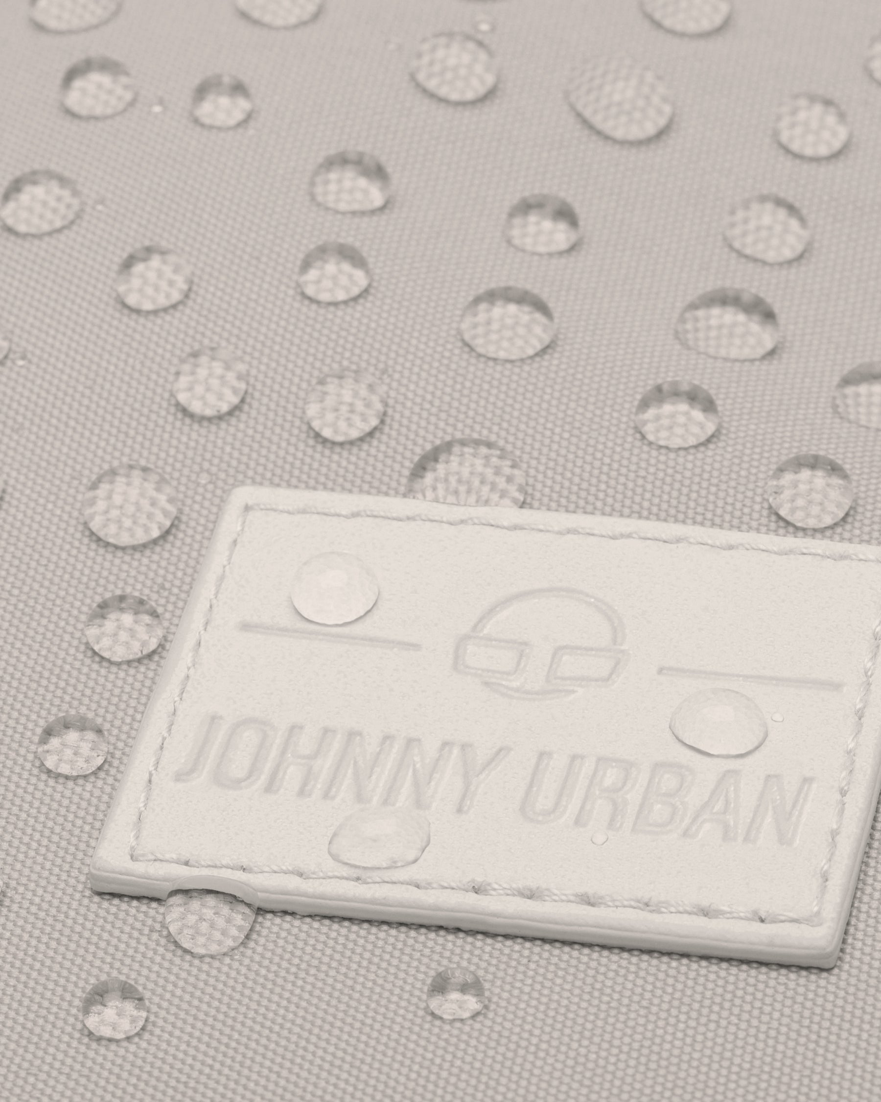 Nahaufnahme des beigen Rucksacks 'Jona Large' mit Wasserperlen auf wasserabweisendem Stoff und Johnny Urban Logo