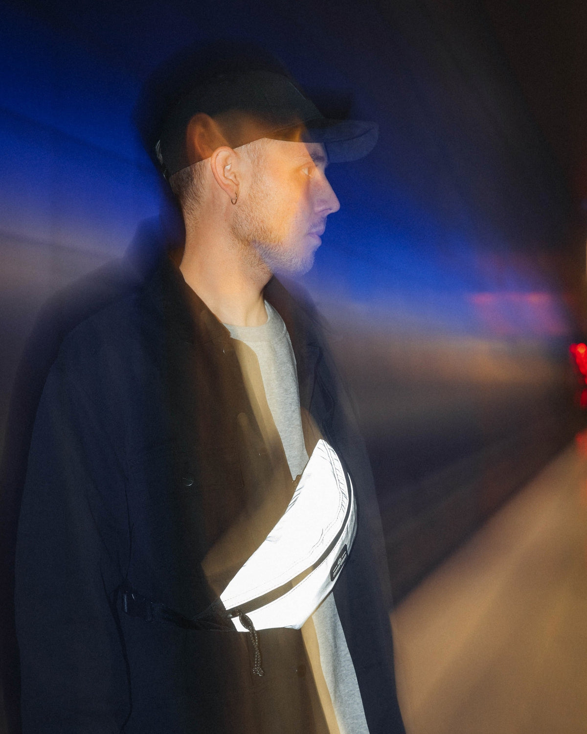 Mann mit reflektierender Bauchtasche 'Erik Small' von Johnny Urban, trägt schwarze Jacke und graues Shirt