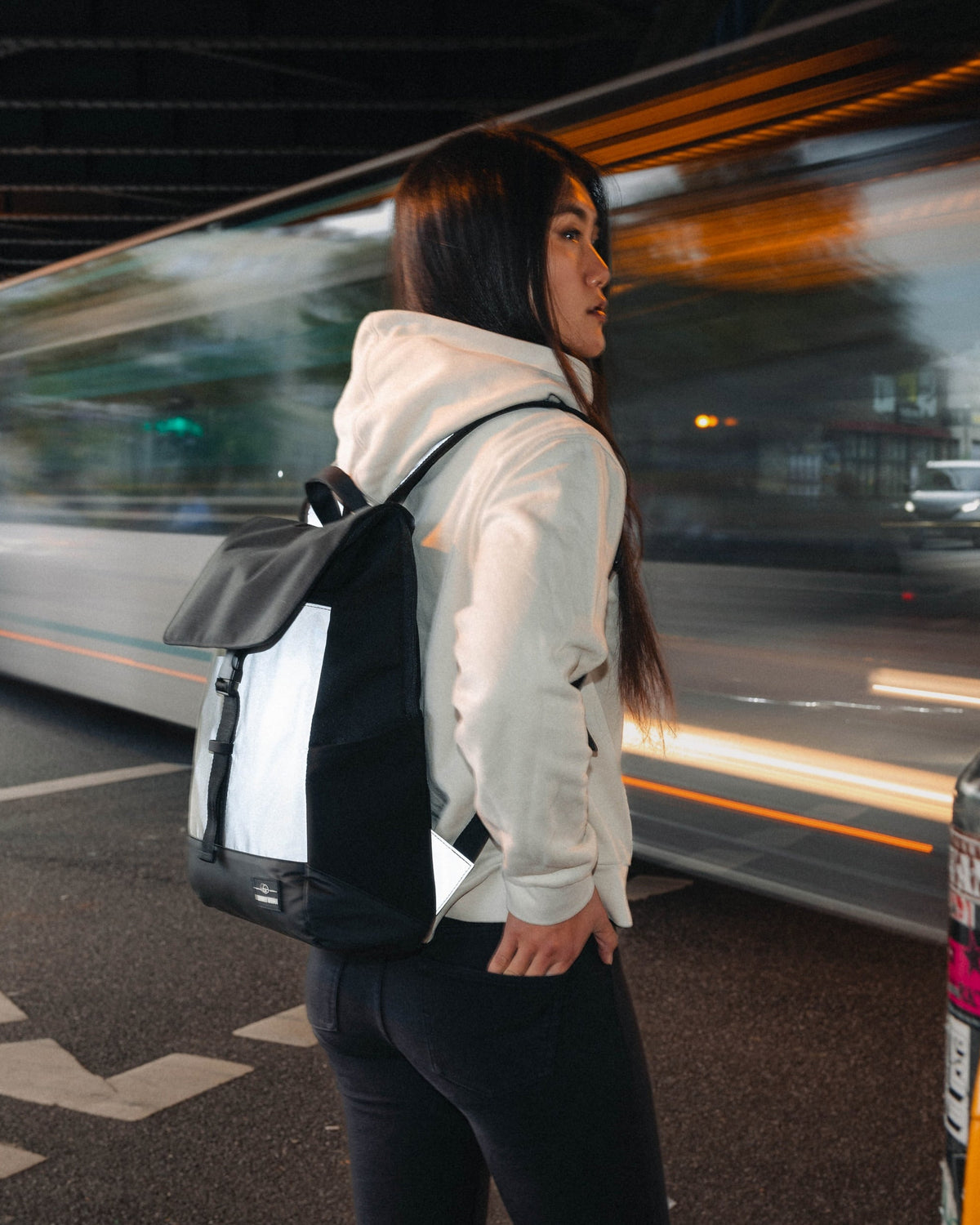 Frau mit reflektierendem Rucksack 'Mika' in Schwarz-Weiß neben einer vorbeifahrenden Straßenbahn