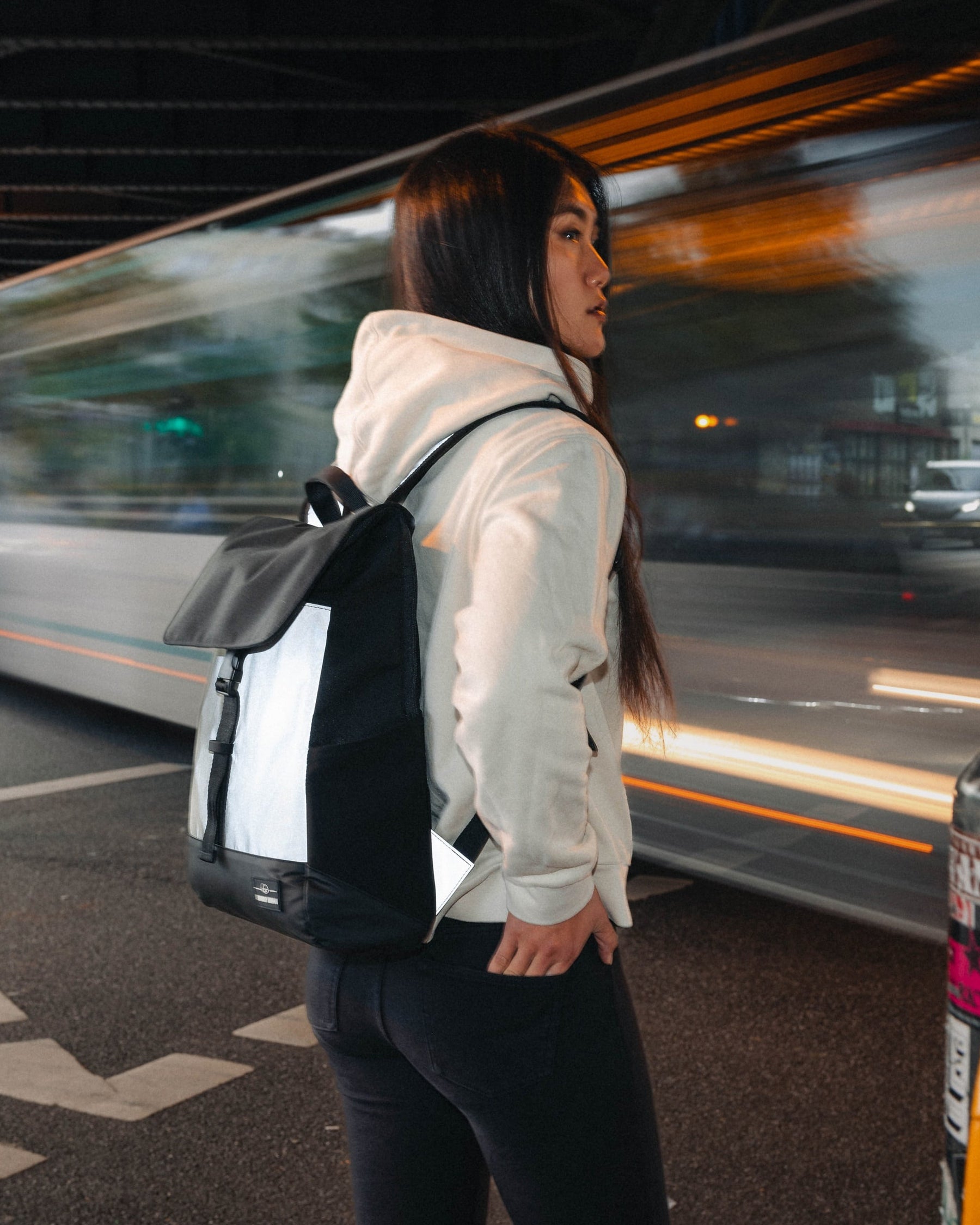 Frau mit reflektierendem Rucksack 'Mika' in Schwarz-Weiß neben einer vorbeifahrenden Straßenbahn