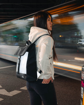 Frau mit reflektierendem Rucksack 'Mika' in Schwarz-Weiß neben einer vorbeifahrenden Straßenbahn