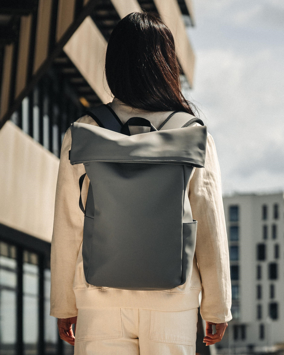Dame von hinten mit hellem Outfit trägt grauen Rolltop-Rucksack 'Henry' von Johnny Urban in urbaner Umgebung