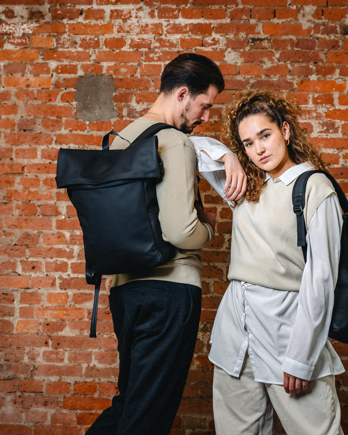 Mann und Frau tragen schwarzen Rolltop Rucksack 'Henry' von Johnny Urban vor Ziegelsteinwand