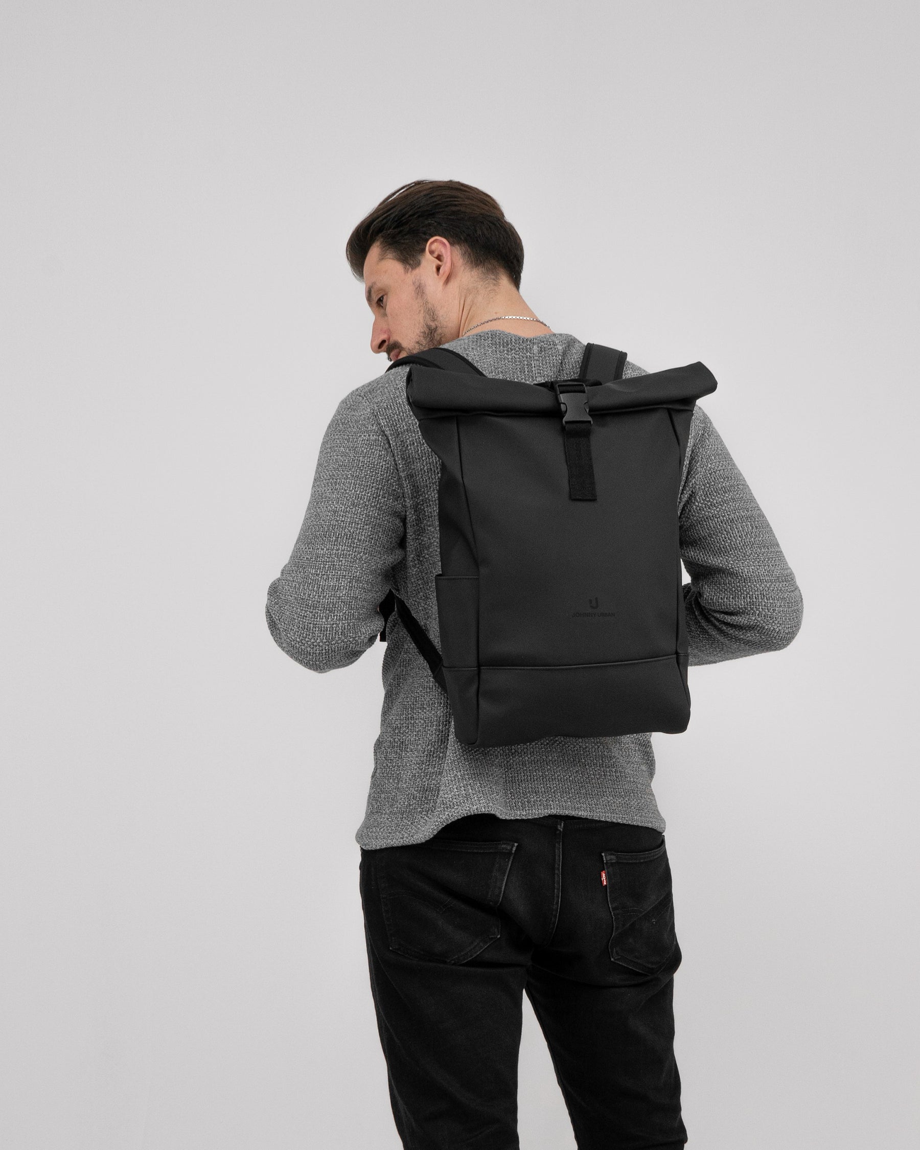 Mann von hinten trägt schwarzen Rolltop-Rucksack 'Harvey Medium' über grauem Pullover und schwarzer Jeans