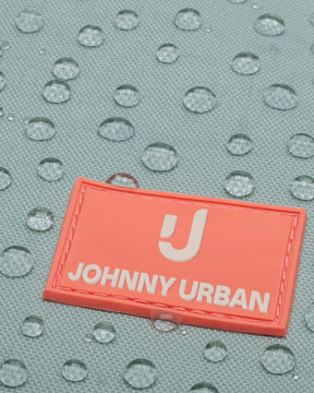 Nahaufnahme des wasserabweisenden Materials des hellblauen Rolltop Kinderrucksacks 'Aaron' mit einem orangefarbenen Johnny Urban Junior Logo.