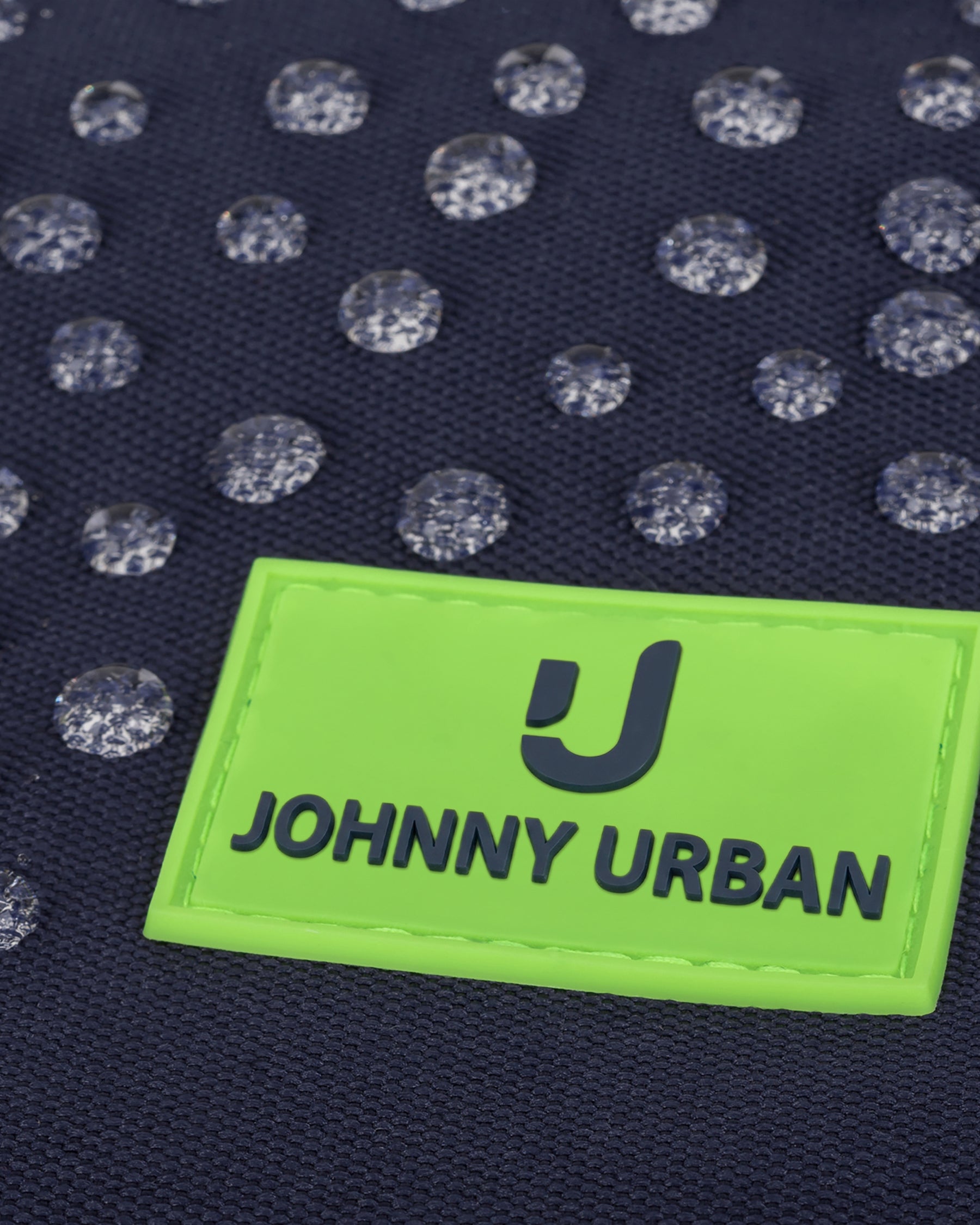 Wasserdichte dunkelblaue Oberfläche mit grüner Marke 'Johnny Urban Junior' und Wassertröpfchen
