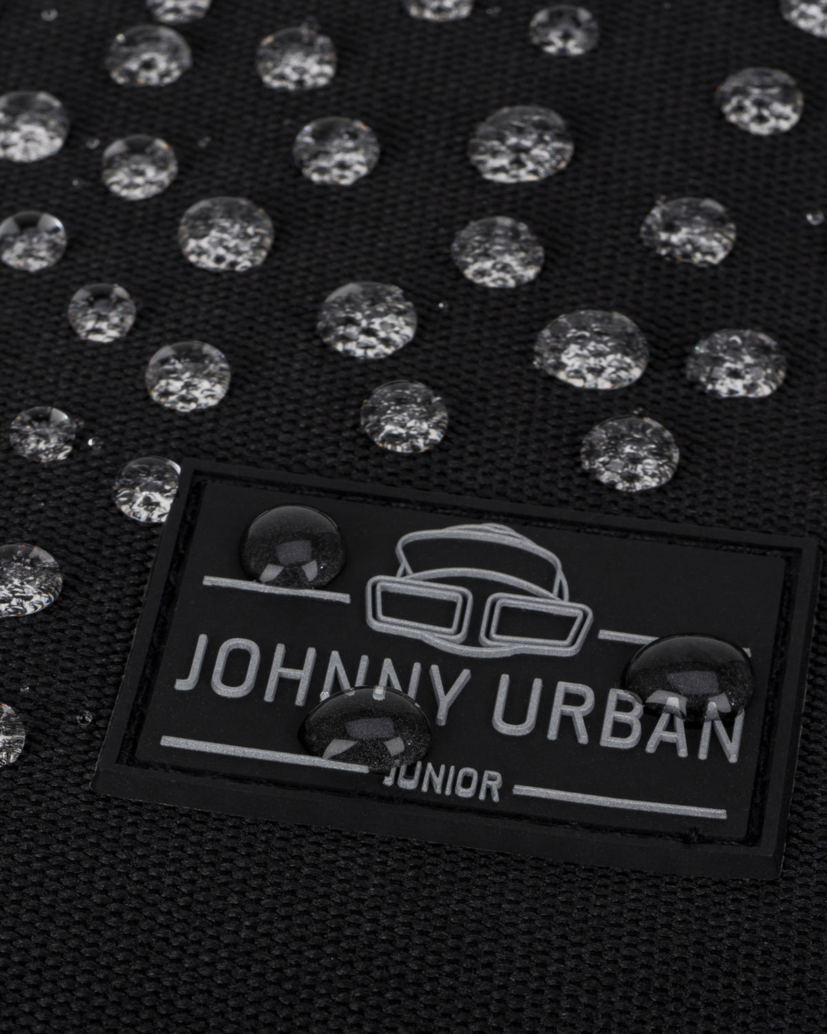 Nahaufnahme eines schwarzen wasserdichten Rolltop Kinderrucksacks 'Aaron' mit Johnny Urban Junior Logo und Wasserperlen