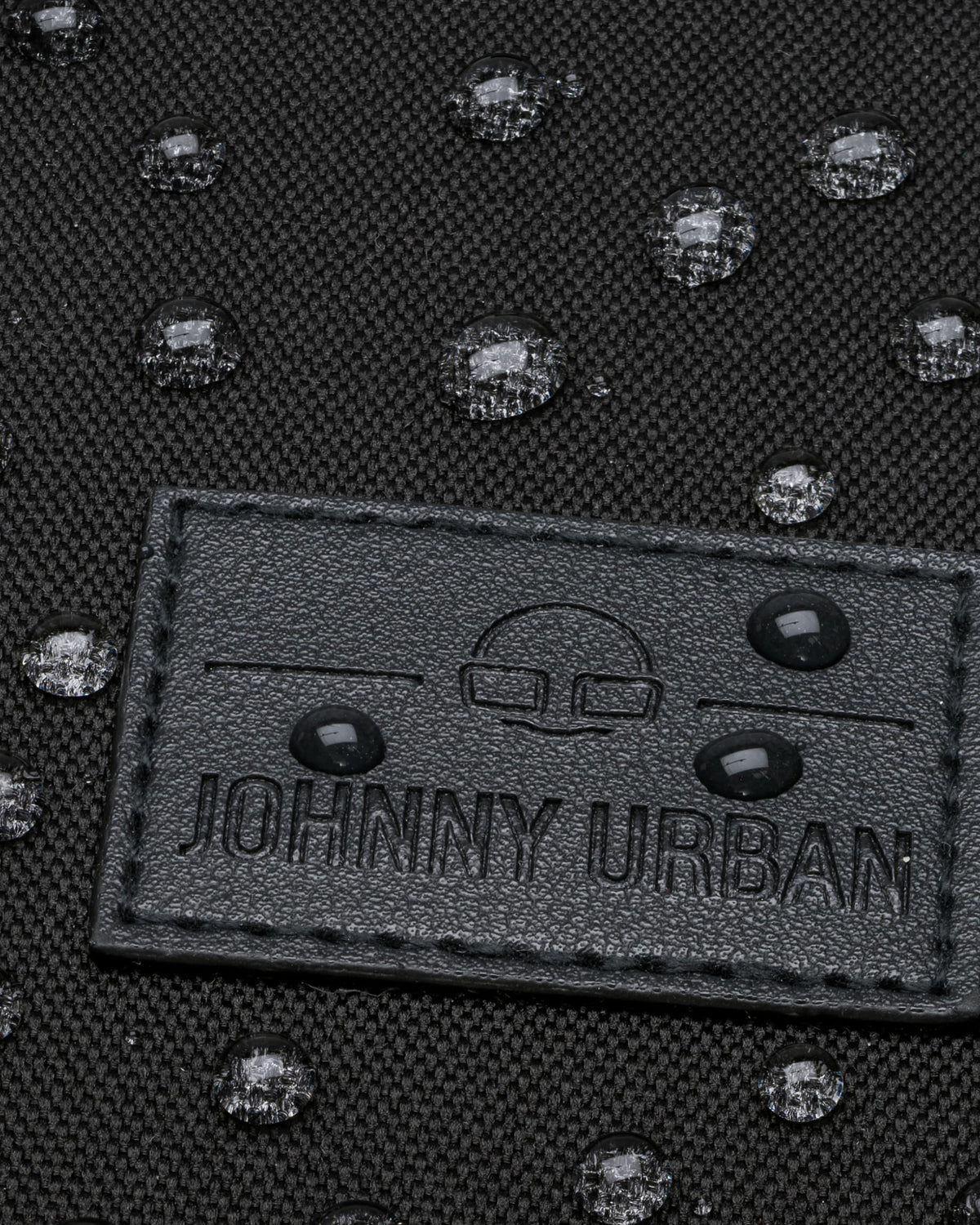 Schwarzes wasserabweisendes Material mit aufgenähtem Johnny Urban Logo-Patch und Wassertropfen