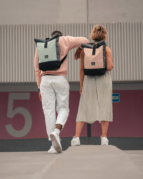 Zwei Personen von hinten mit Rolltop Rucksack 'Ryan' in Pastellfarben, stehend vor einer Wand mit großer Zahl 5